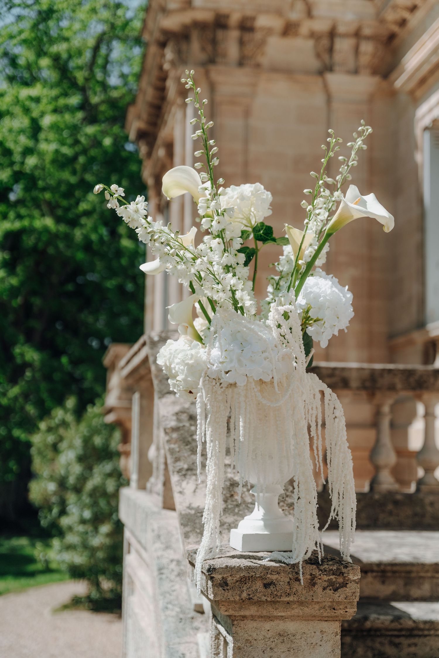 Elegant white floral arrangements with lilies and baby's breath in glass vases on stone ledge.