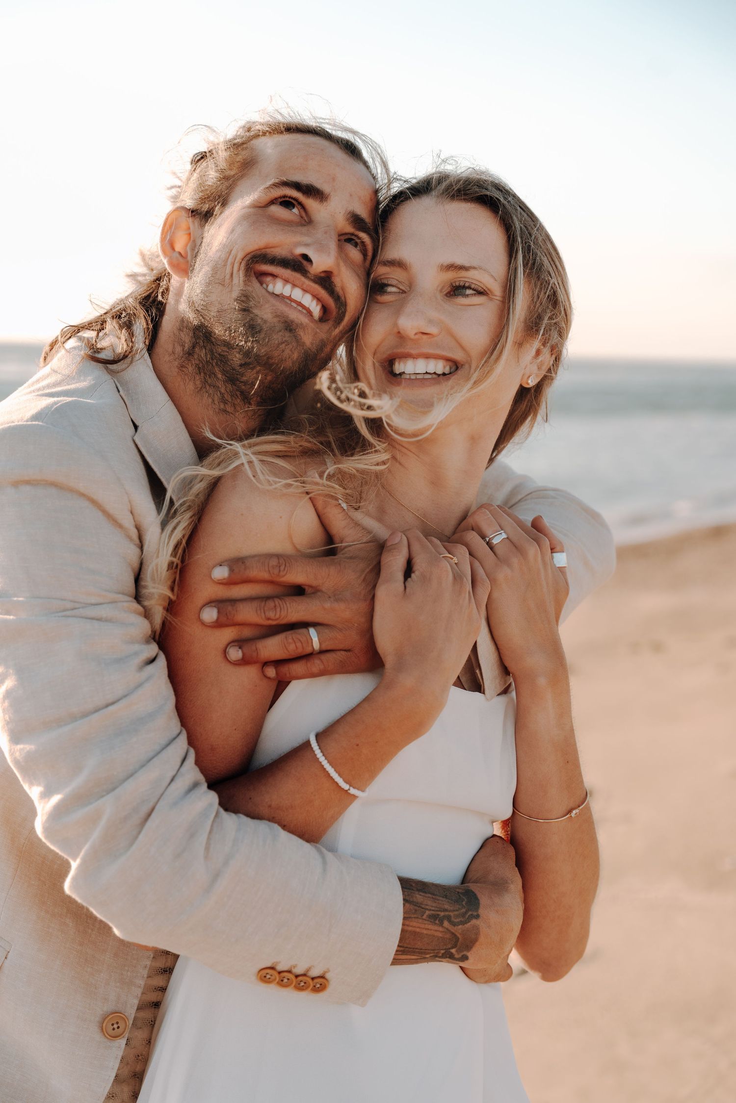 Joyful couple embracing and laughing on sandy beach at sunset.