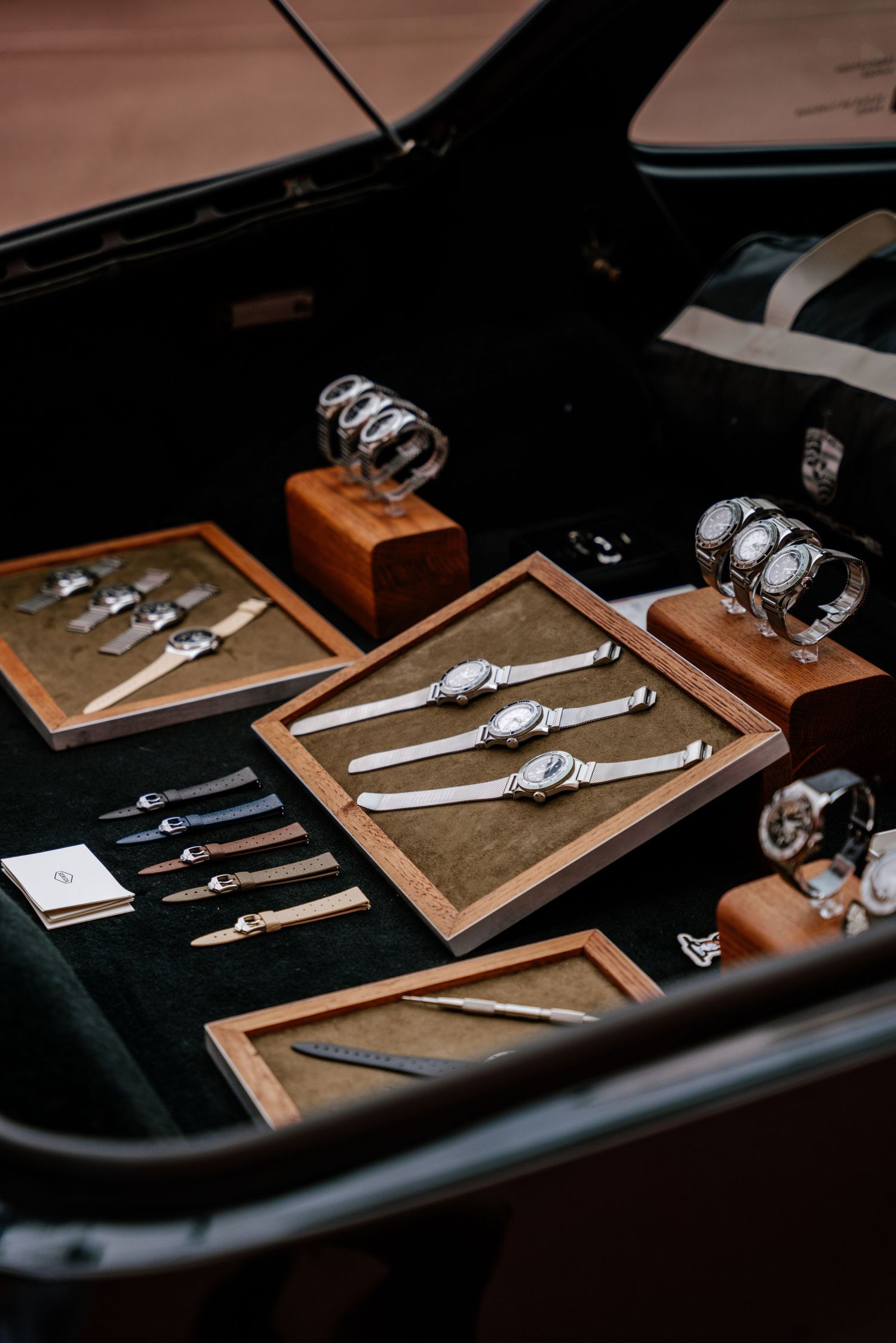 Luxury watches and writing instruments displayed on dark velvet surface with wooden presentation boxes in moody lighting.