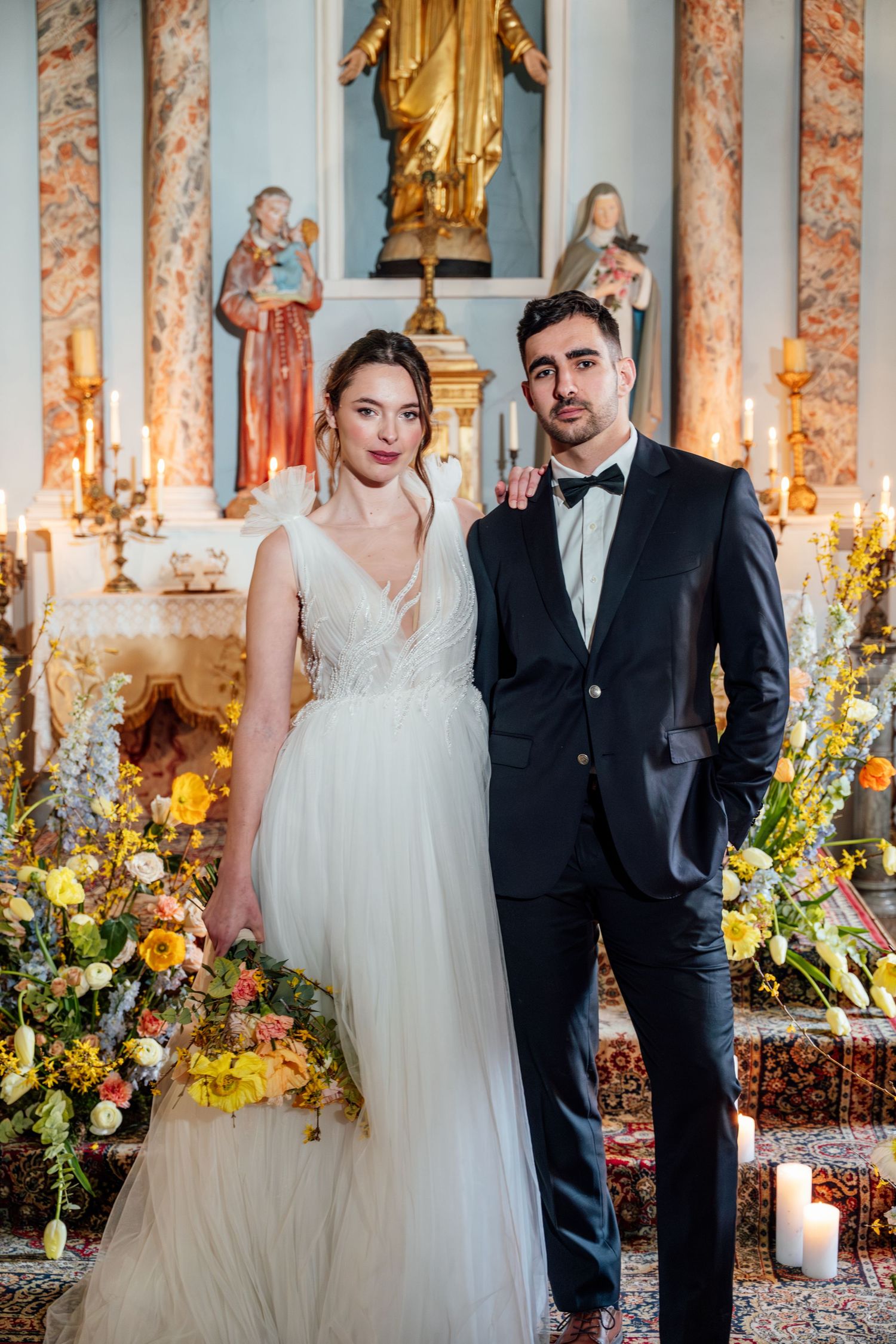 Wedding couple posing in an elegant church interior with ornate marble columns and floral arrangements.