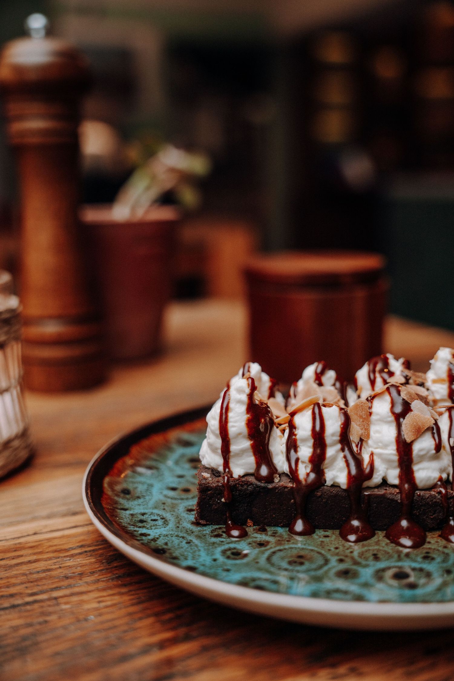 A decadent chocolate brownie topped with whipped cream and chocolate drizzle served on a turquoise decorative plate.