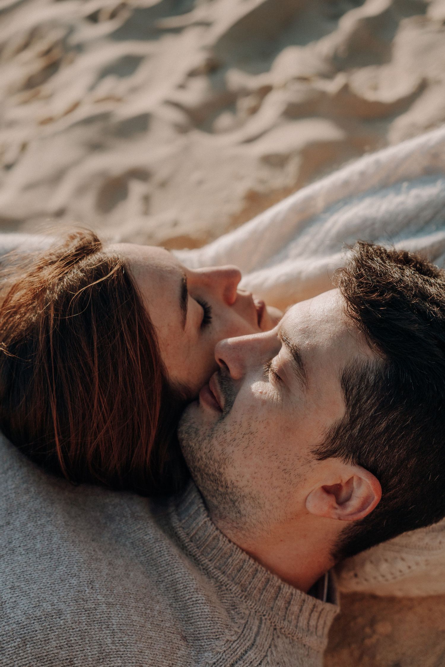 A couple lies close together on sandy beach during an intimate photoshoot.
