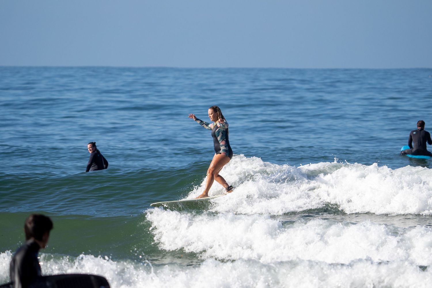 A surfer rides a wave in the ocean while others watch from the water.