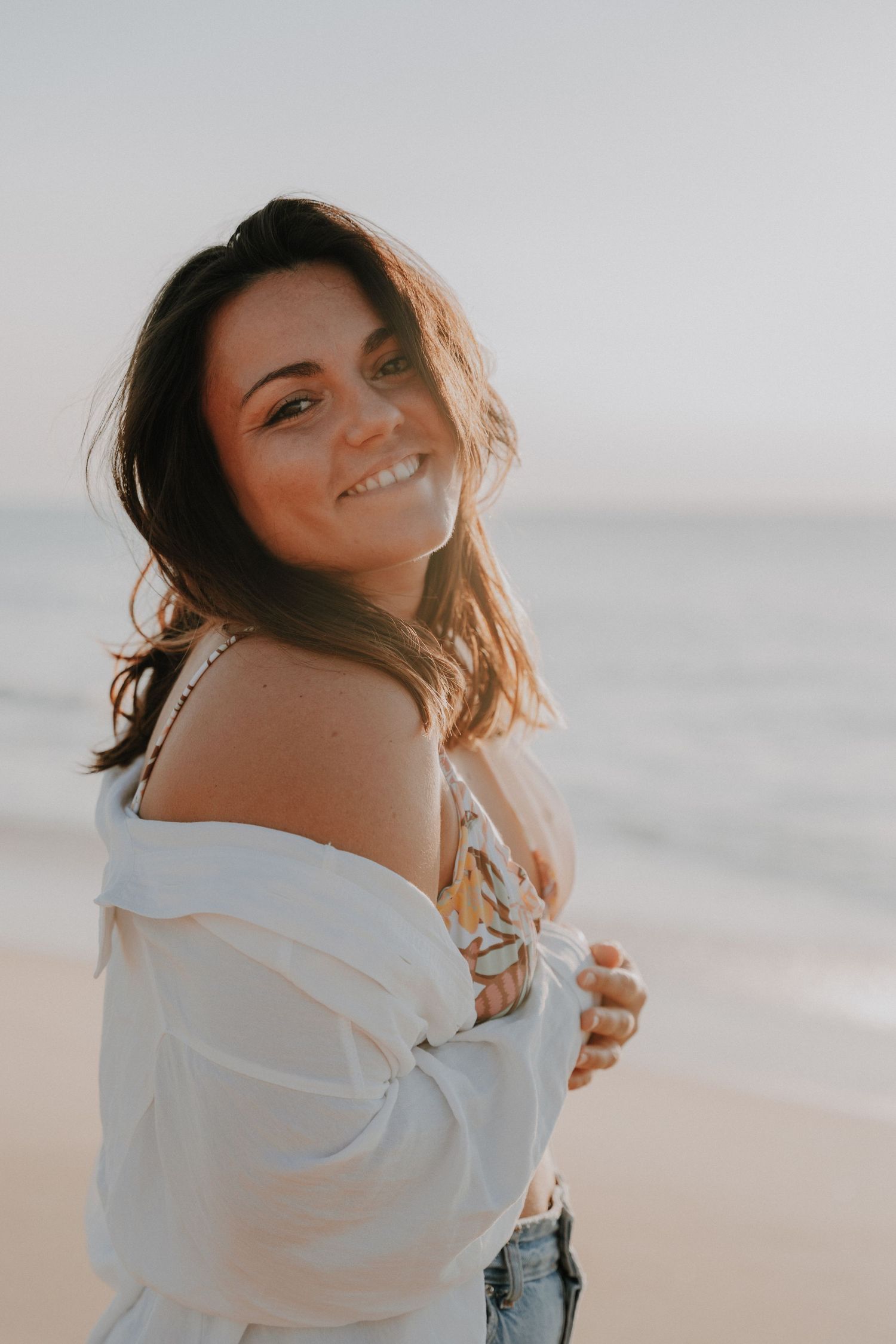 Portrait series of someone in a white sweater posing against a bright background at the beach.