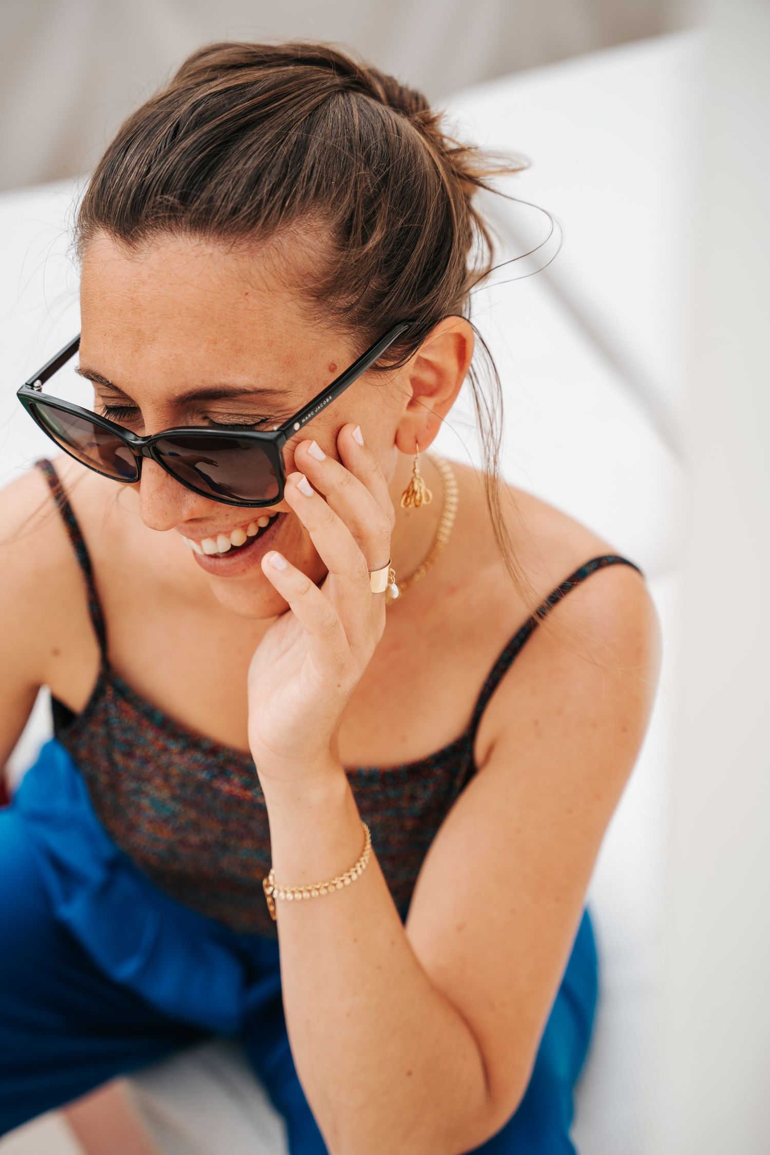 Person wearing sunglasses and mask covers their face with their hand while showing signs of distress or fatigue.