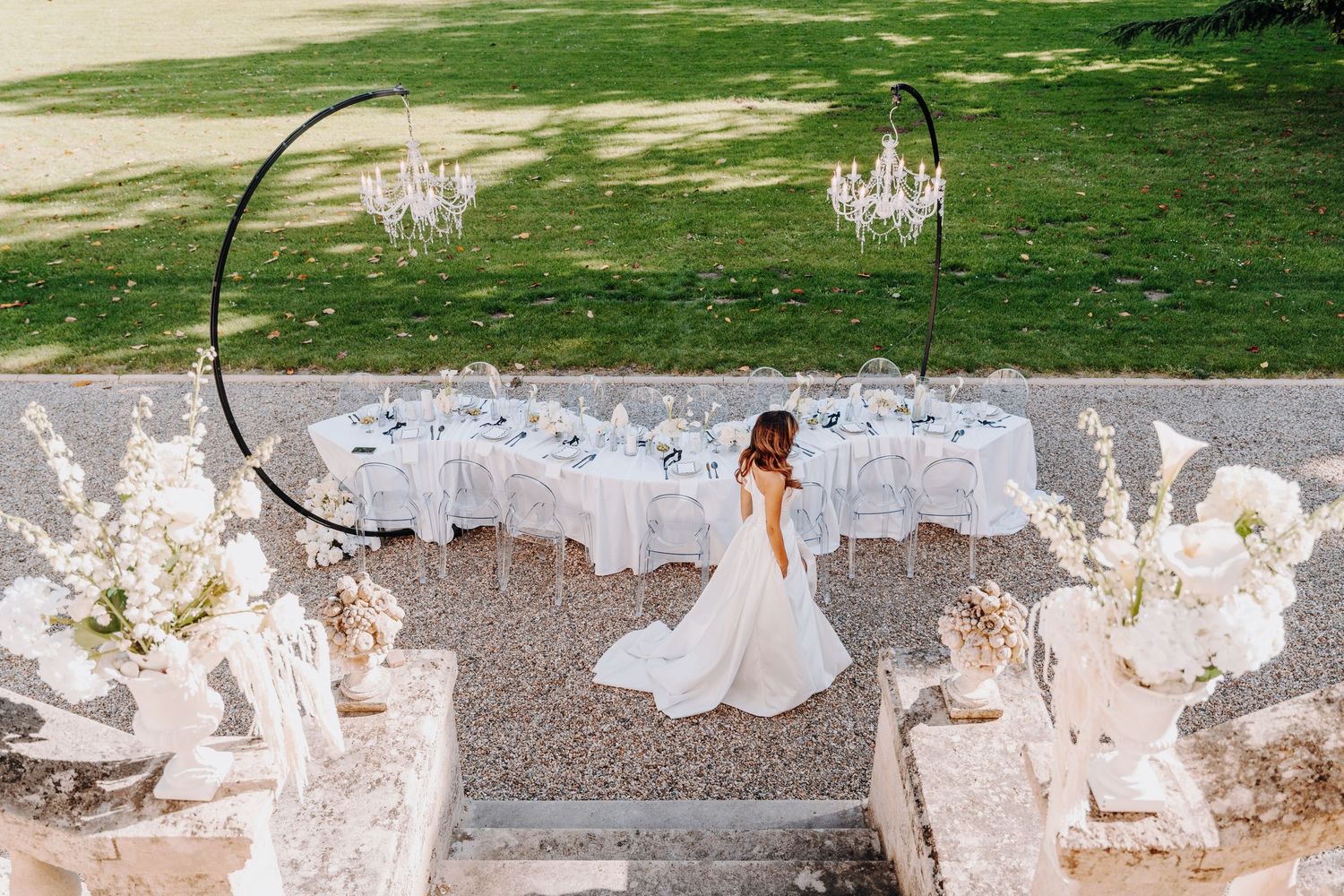 Wedding reception setup on lawn with chandeliers and white decor against mansion backdrop.