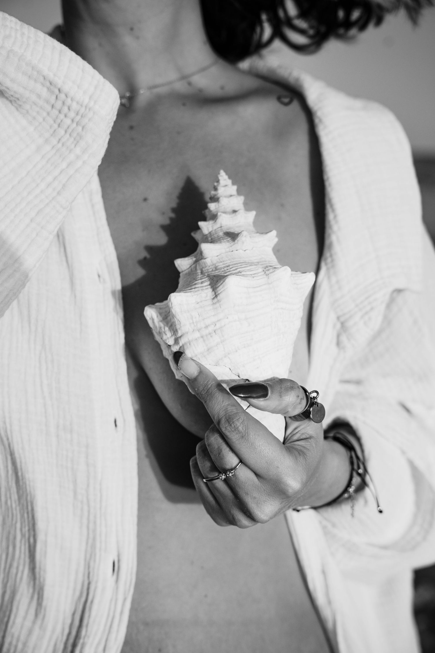 Black and white photo of hands holding a delicate white seashell conch against a light fabric background.