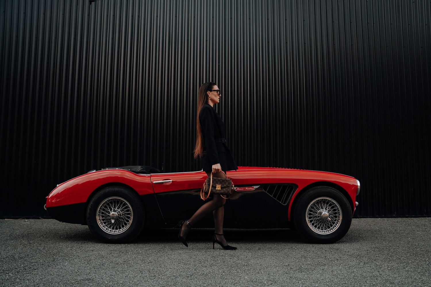 Classic red vintage sports car against dark industrial wall.