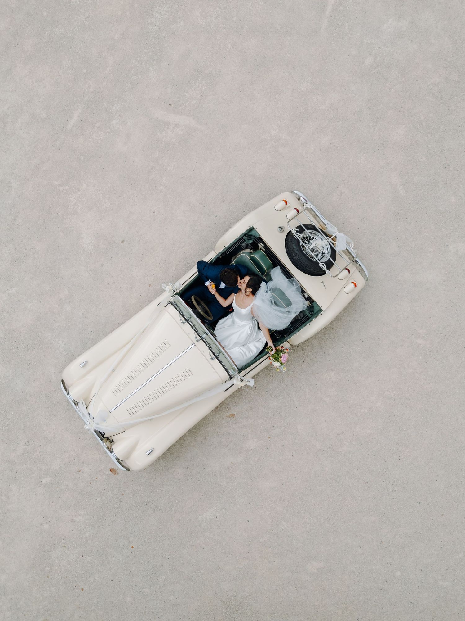Aerial view of newlyweds in vintage white car during wedding celebration.