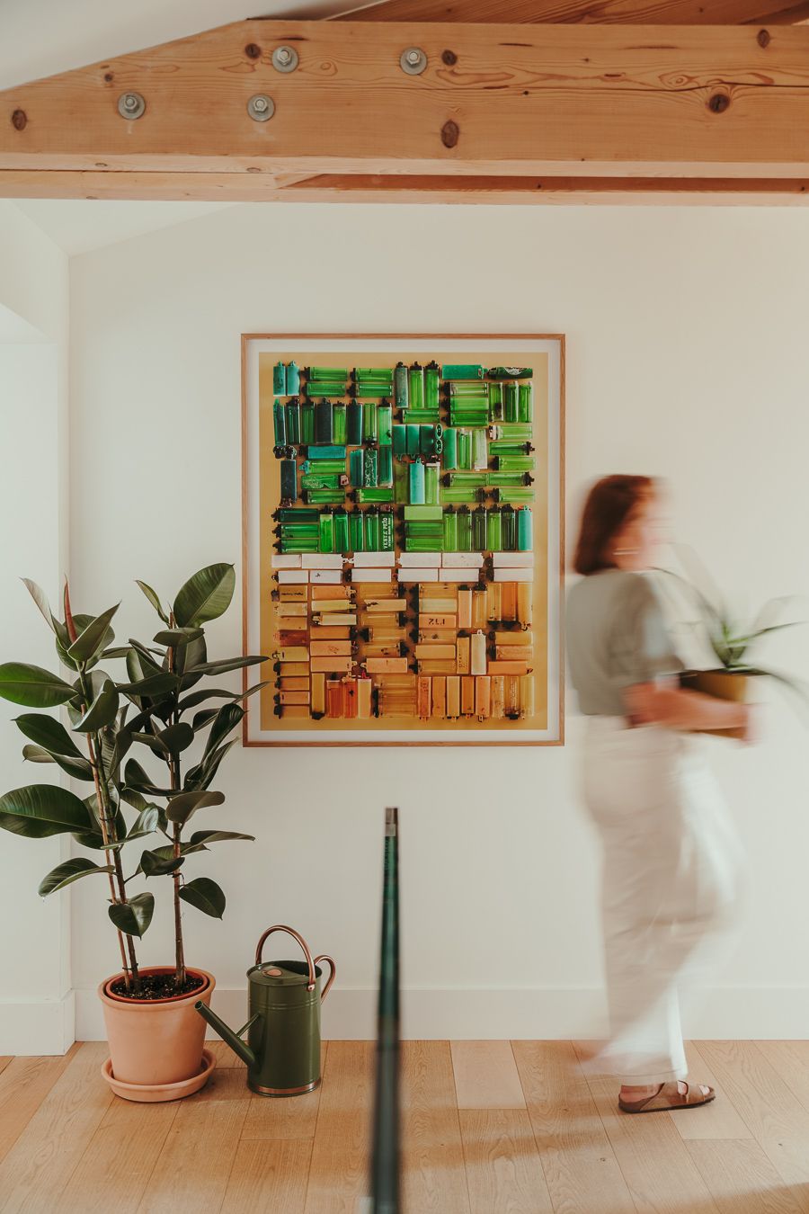 Motion blur of someone walking past green artwork and plants in a minimalist interior with wooden beams and white walls.