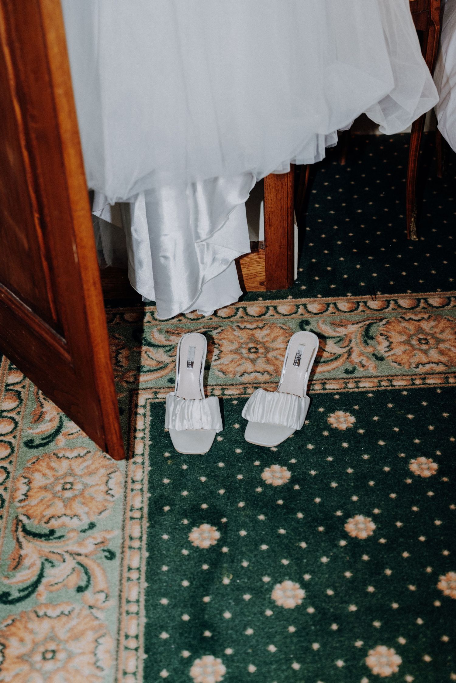Detail shot of white wedding dress and shoes against an elegant patterned carpet.