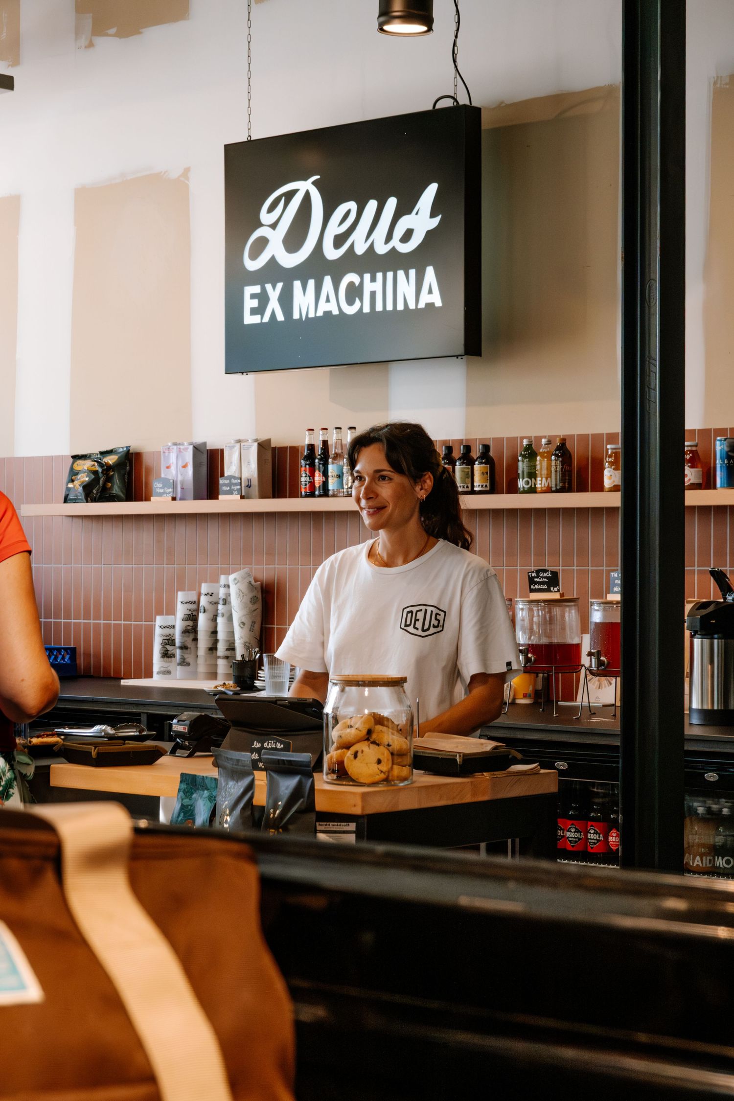 Modern cafe interior with minimalist design and signage reading 'Deus' and 'Ex Machina'.