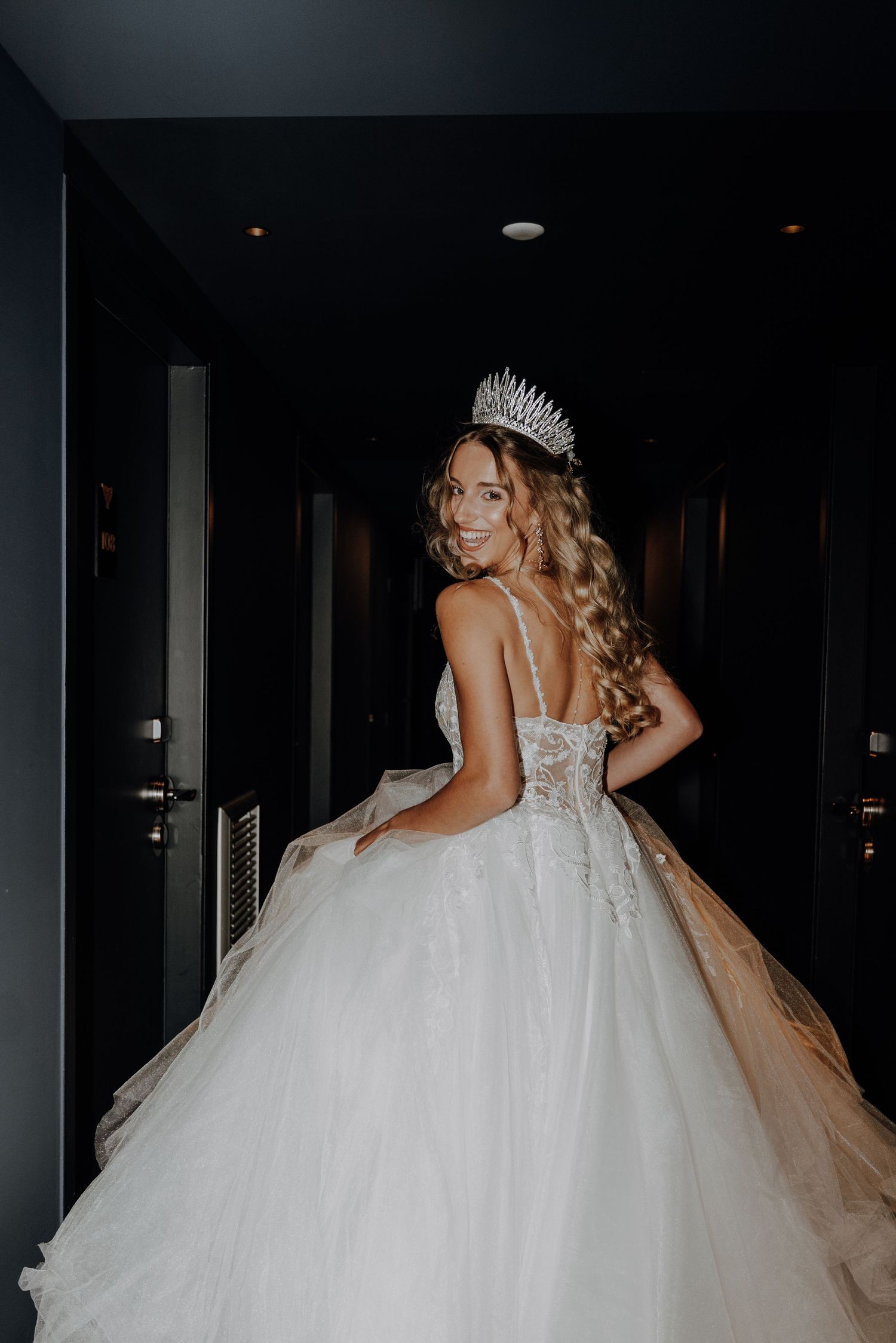 Dramatic silhouette of bride in flowing ballgown dress moving through dark hallway.