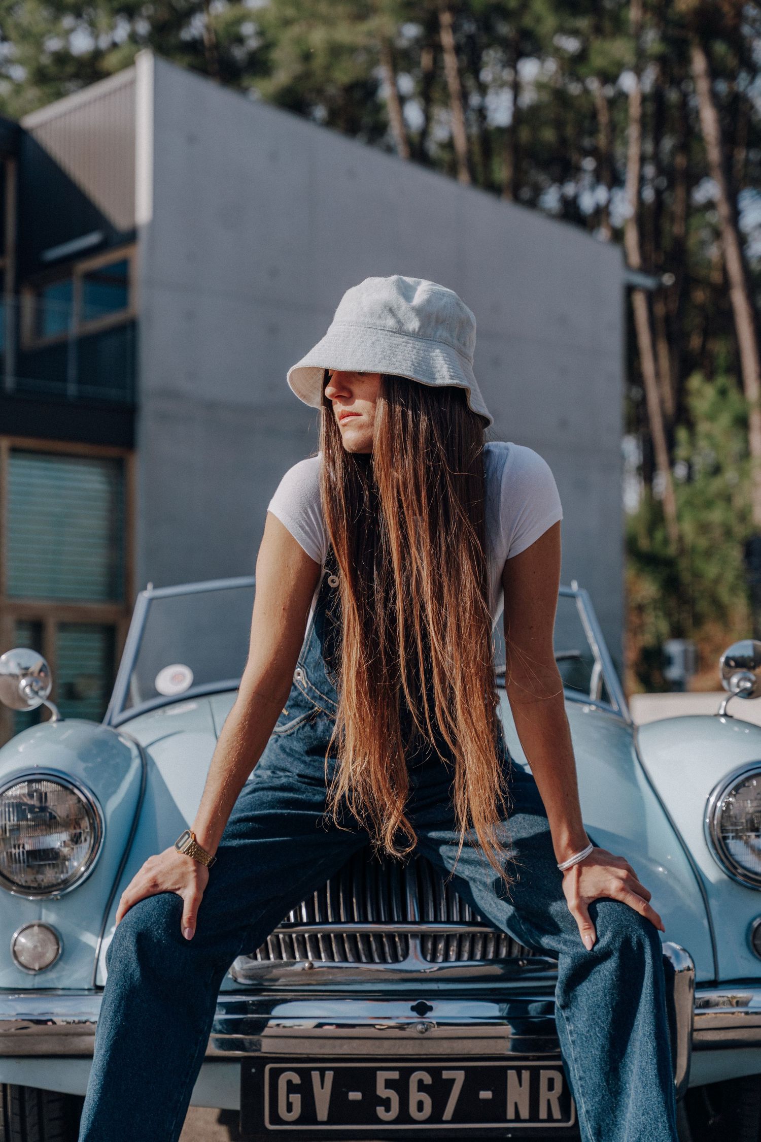 Casual poses with vintage light blue car showing front grille and license plate.