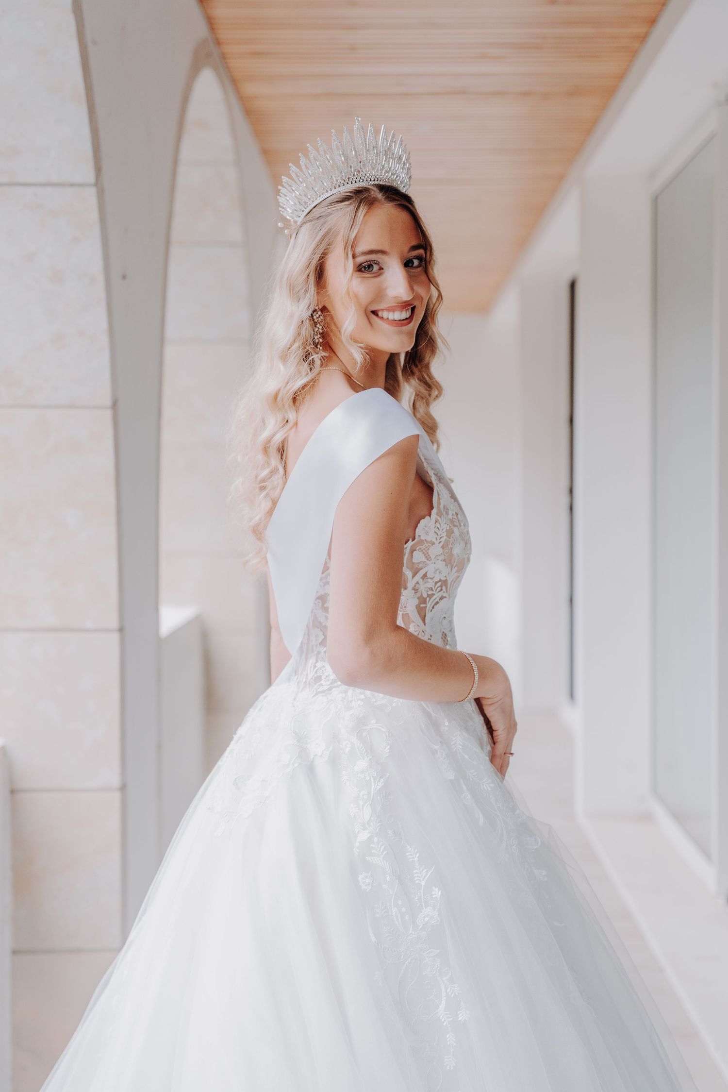 Elegant bridal photos showcasing princess ballgown and tiara in white corridor.