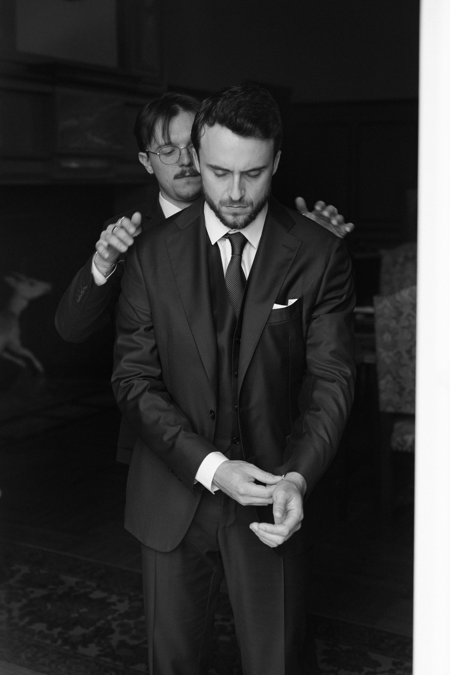 Wedding party members in formal attire gather in dimly lit indoor setting.