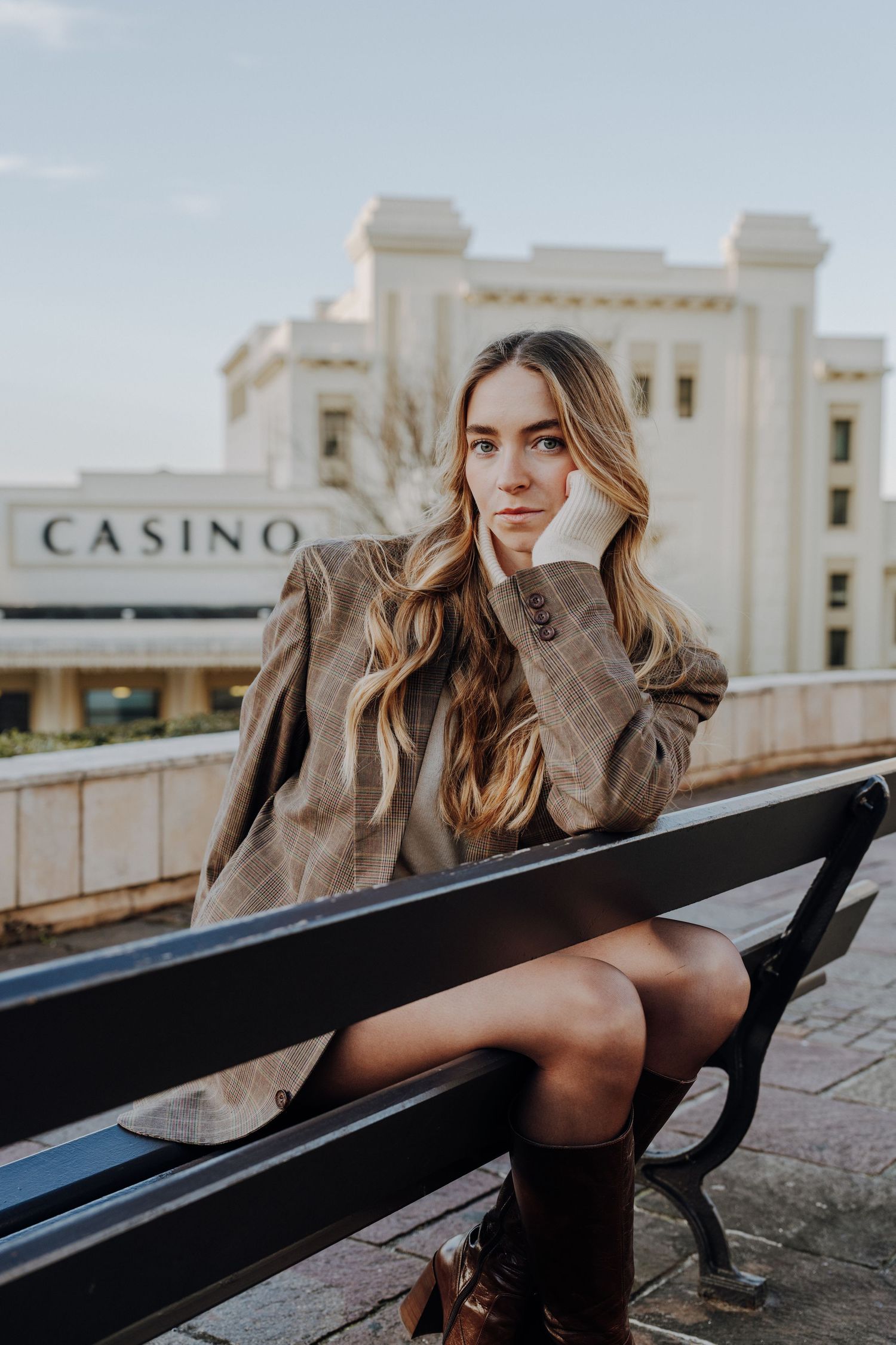 Fashion model posing on bench near casino building in moody lighting.