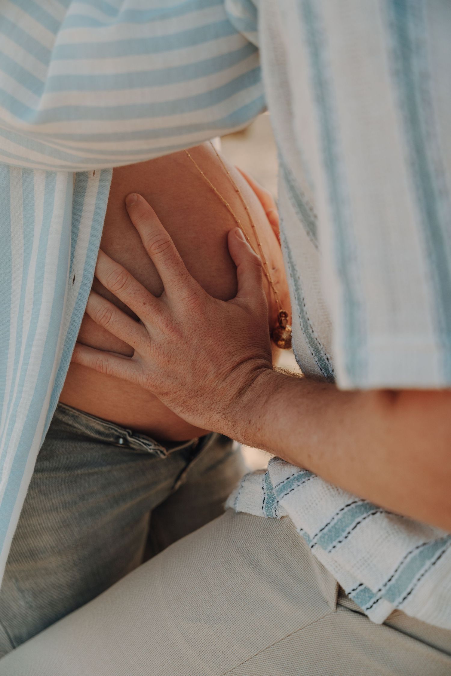 Close up of hands touching bare pregnant belly through striped shirt.