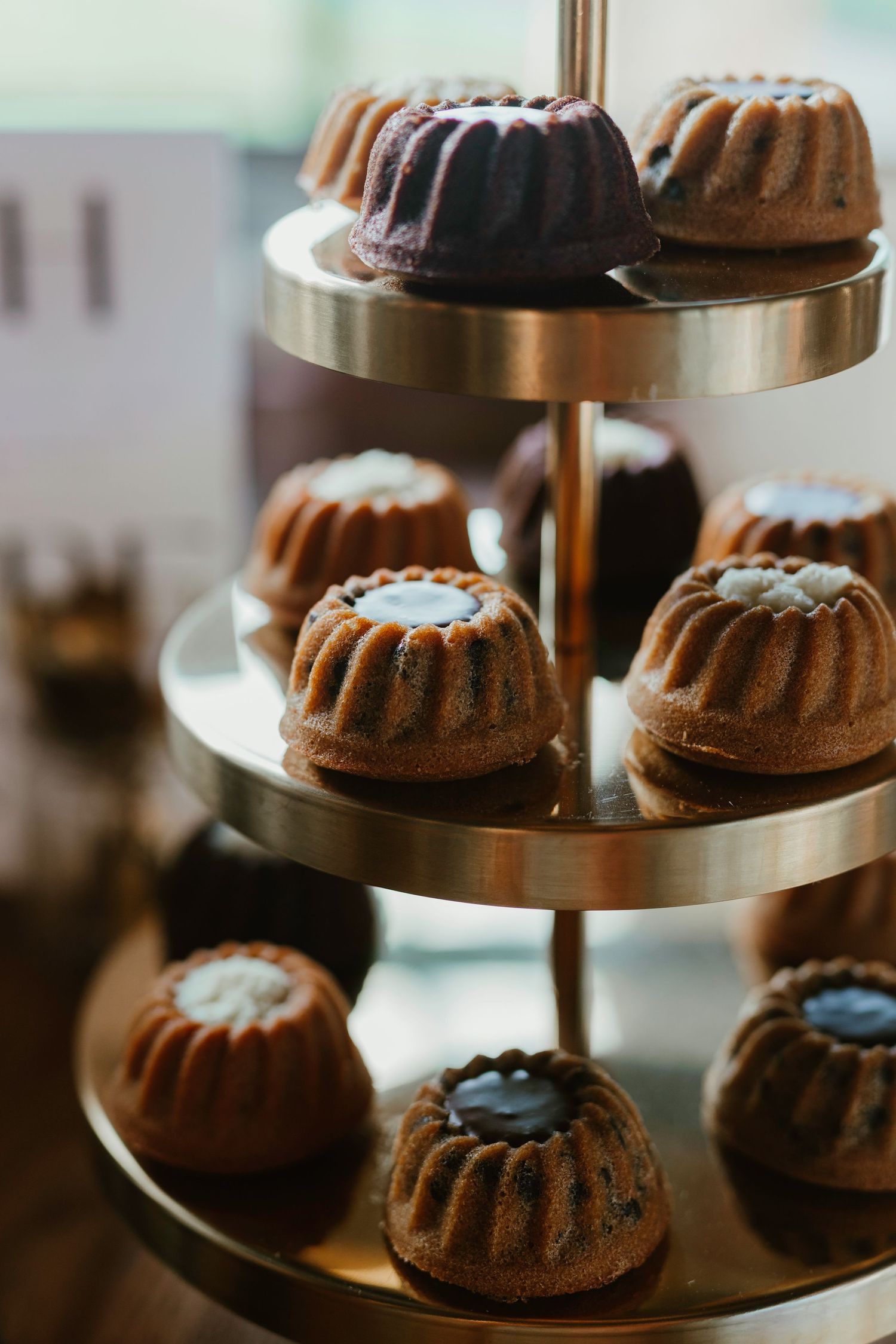 Chocolate bundt cakes displayed on a multi-tiered copper serving stand at a dessert table.