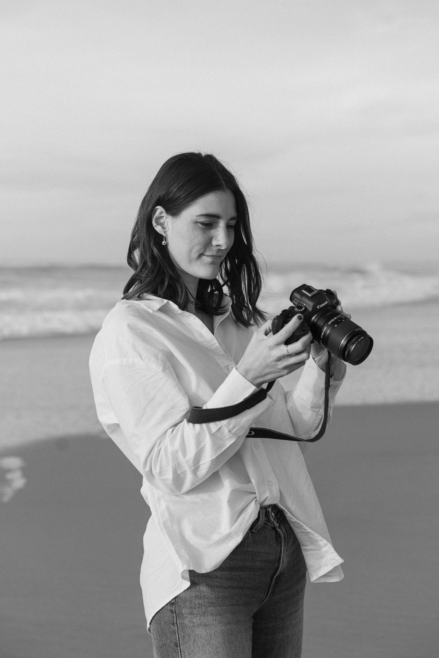 Photographer in white shirt and jeans taking pictures at beach in black and white.