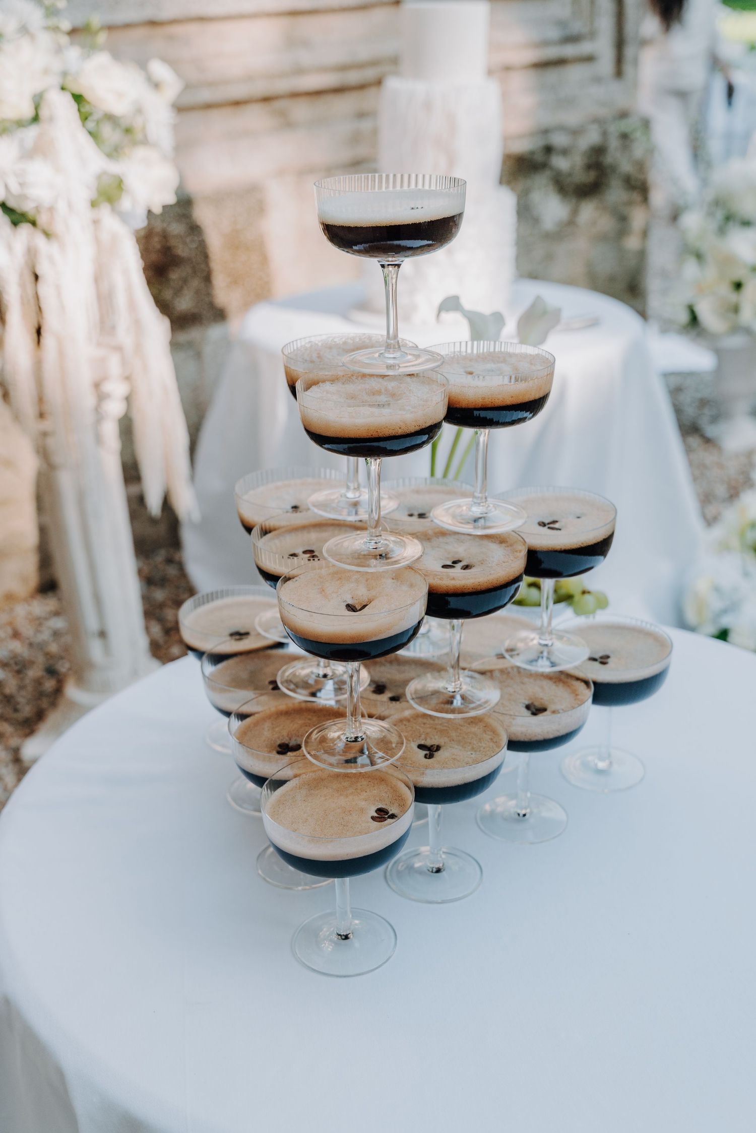 Elegant tower of espresso martini cocktails arranged on a white tablecloth at a wedding reception.