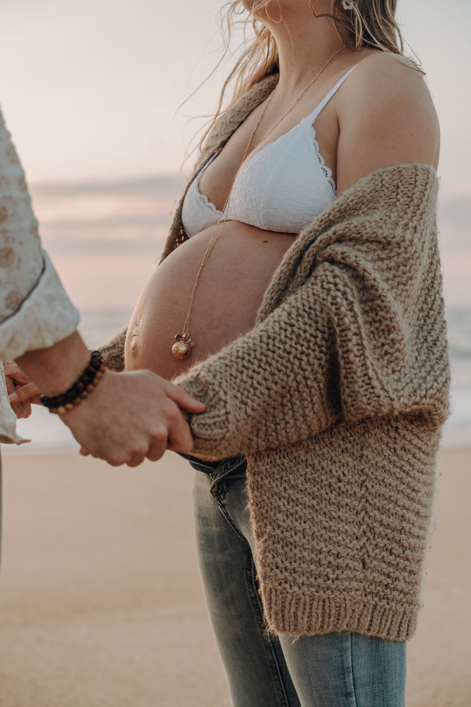 Detail shots of expecting couple wearing knit sweater and casual attire on beach.