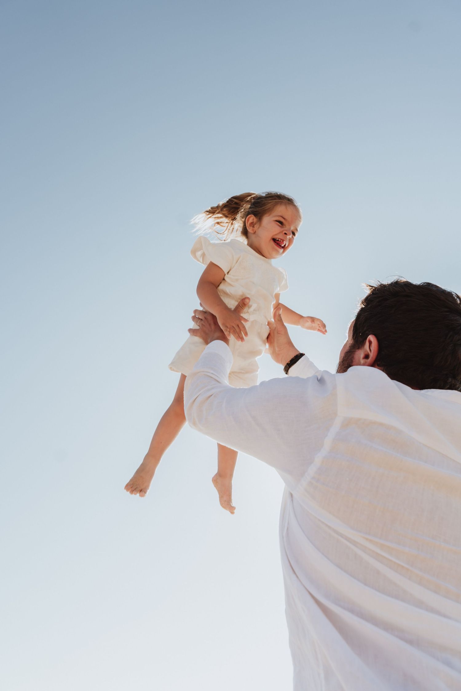 Playful moment captured against bright blue sky in white clothing.