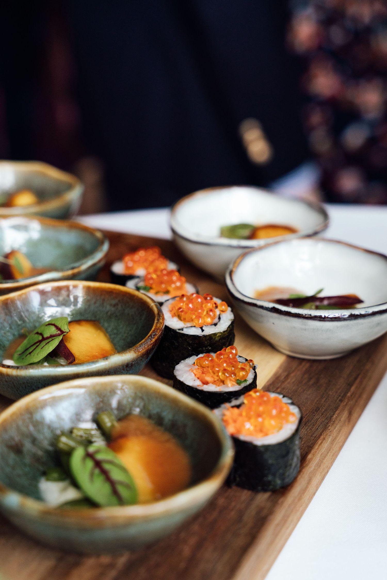 Assorted sushi rolls topped with tobiko caviar served on a wooden board with ceramic bowls at a Japanese restaurant.