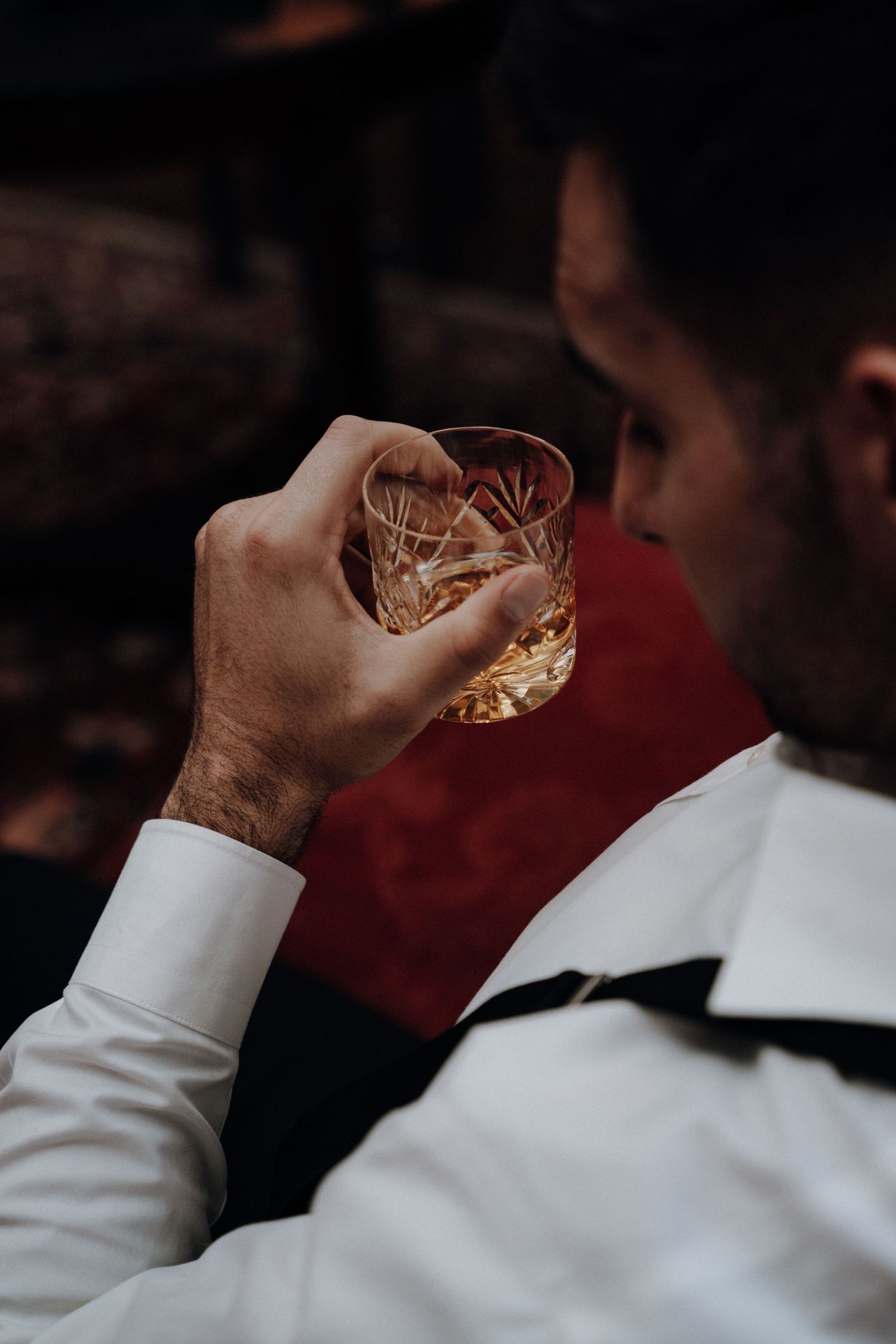 Close-up of hand holding crystal whiskey glass in dimly lit setting.