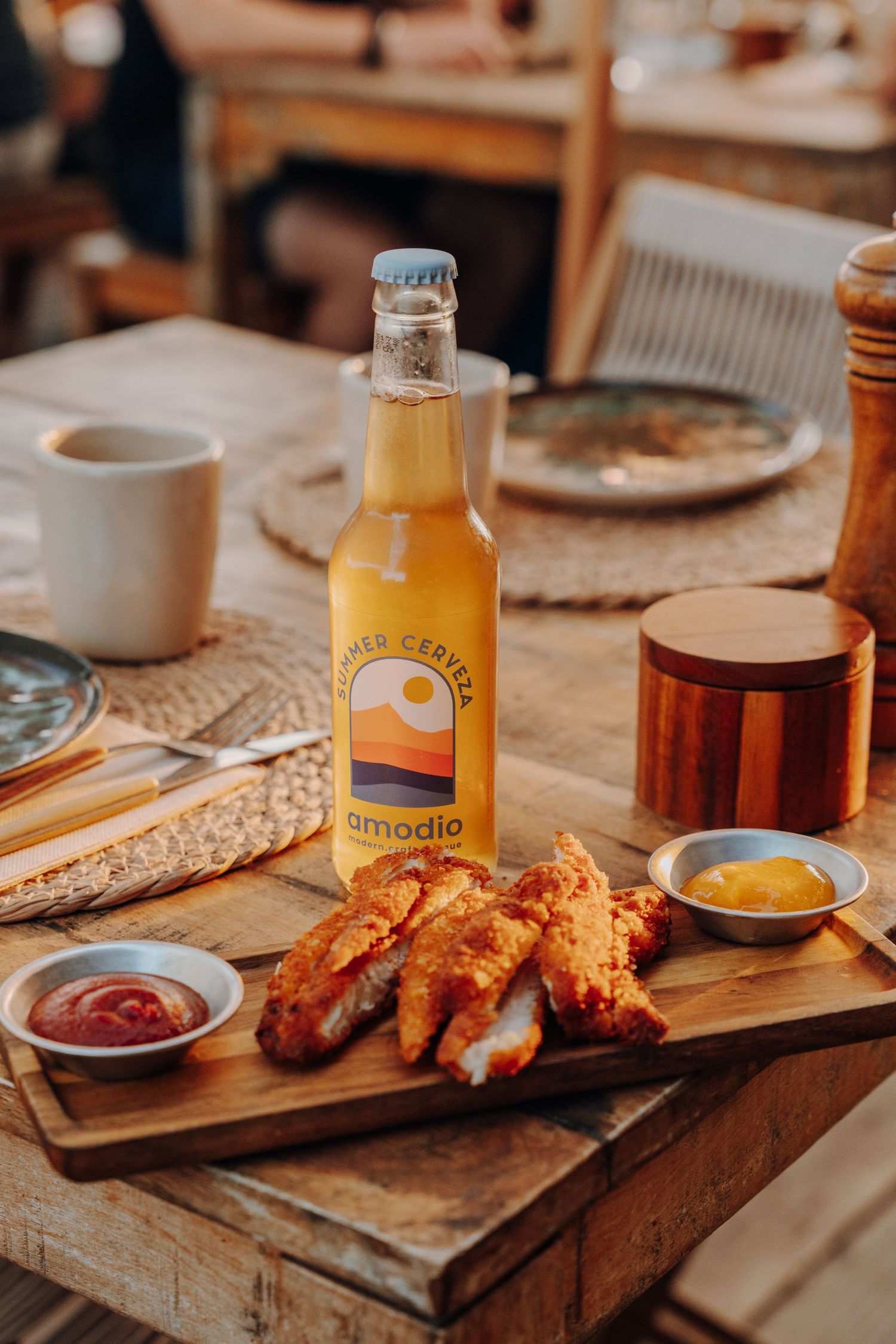 Wooden serving board with crispy fried chicken tenders and dipping sauces alongside a glass bottle of orange juice.