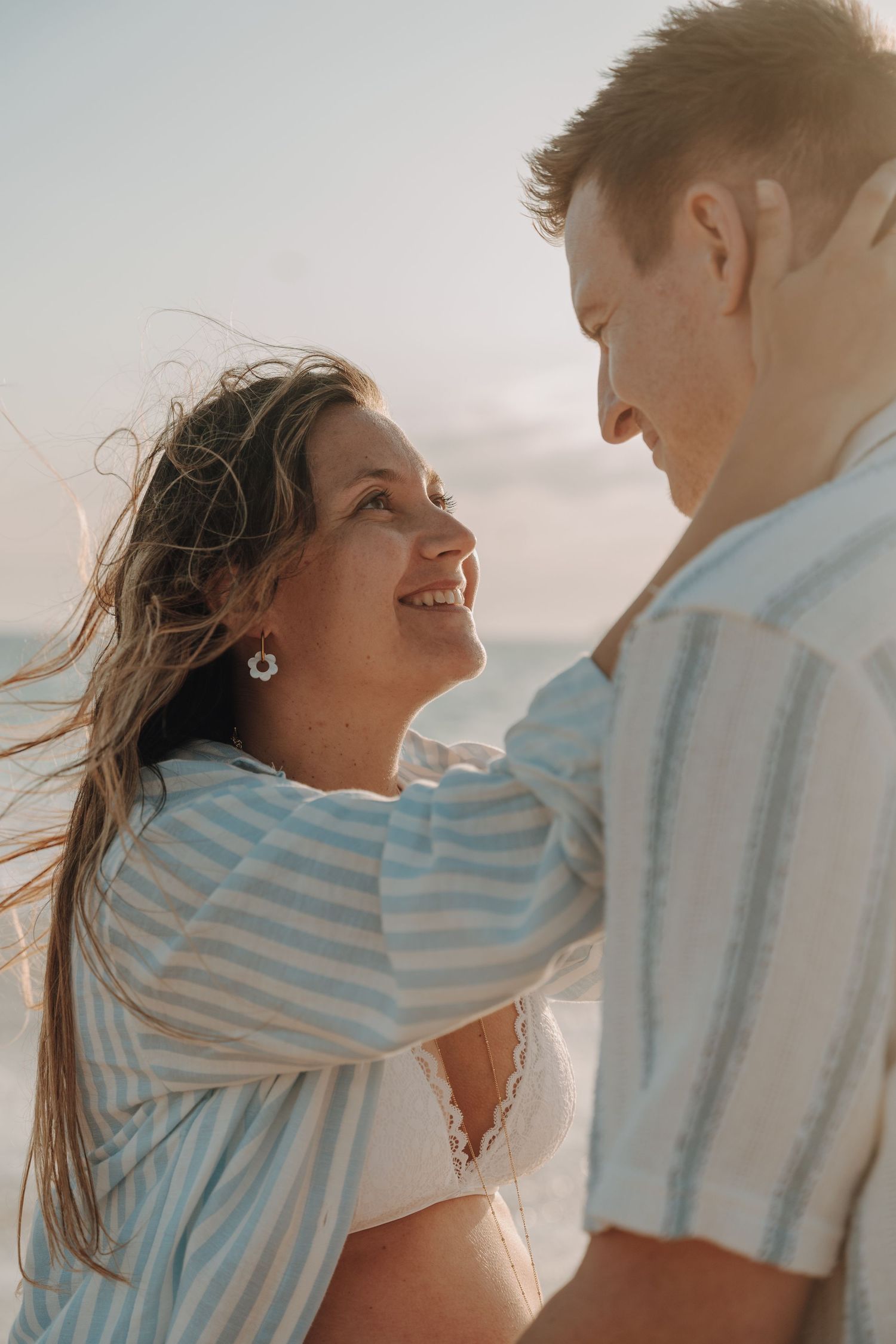 Candid beach photoshoot capturing joyful moments between expecting couple at golden hour.