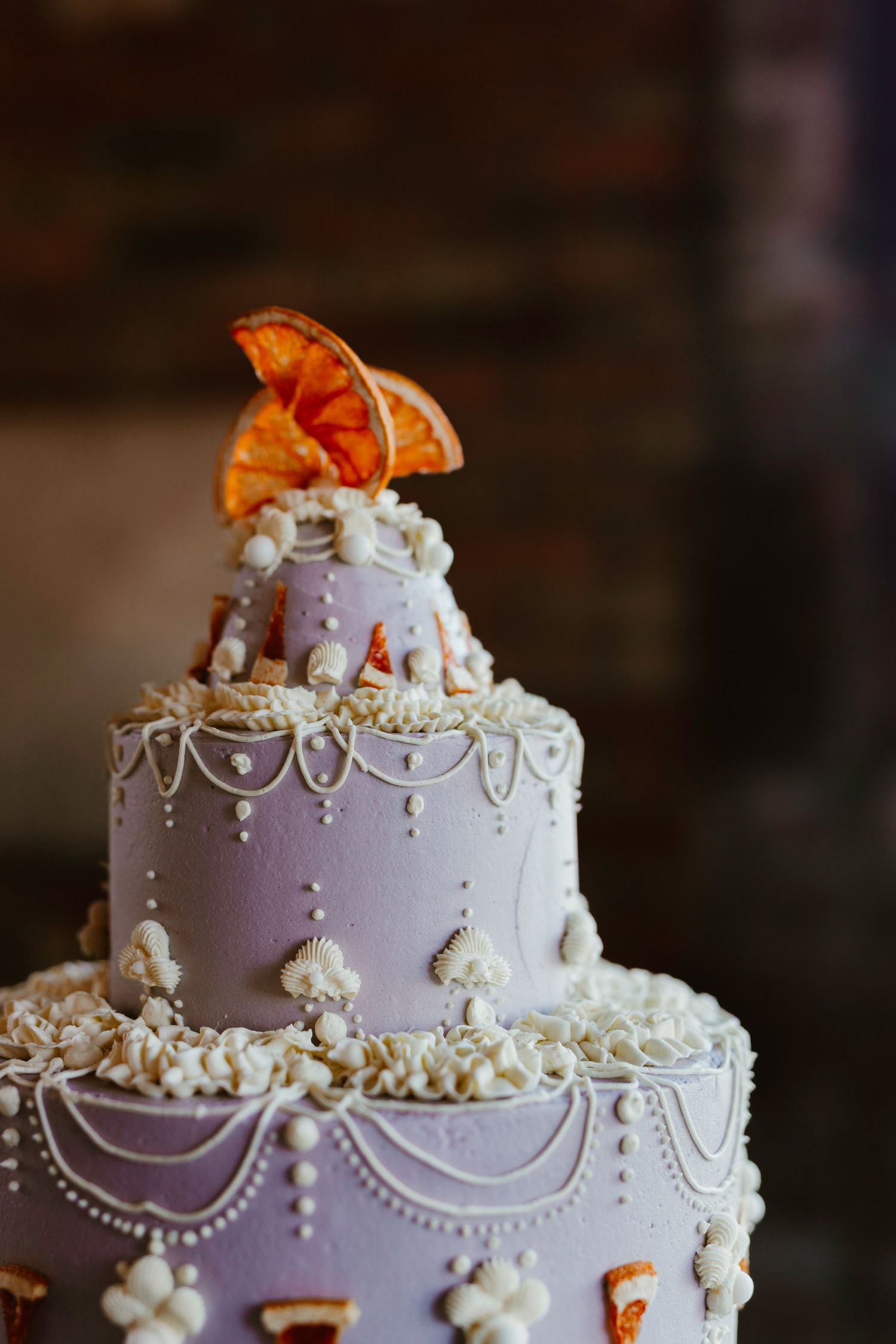 Elegant white wedding cake with delicate piped swags and pearl details topped with orange floral accents.