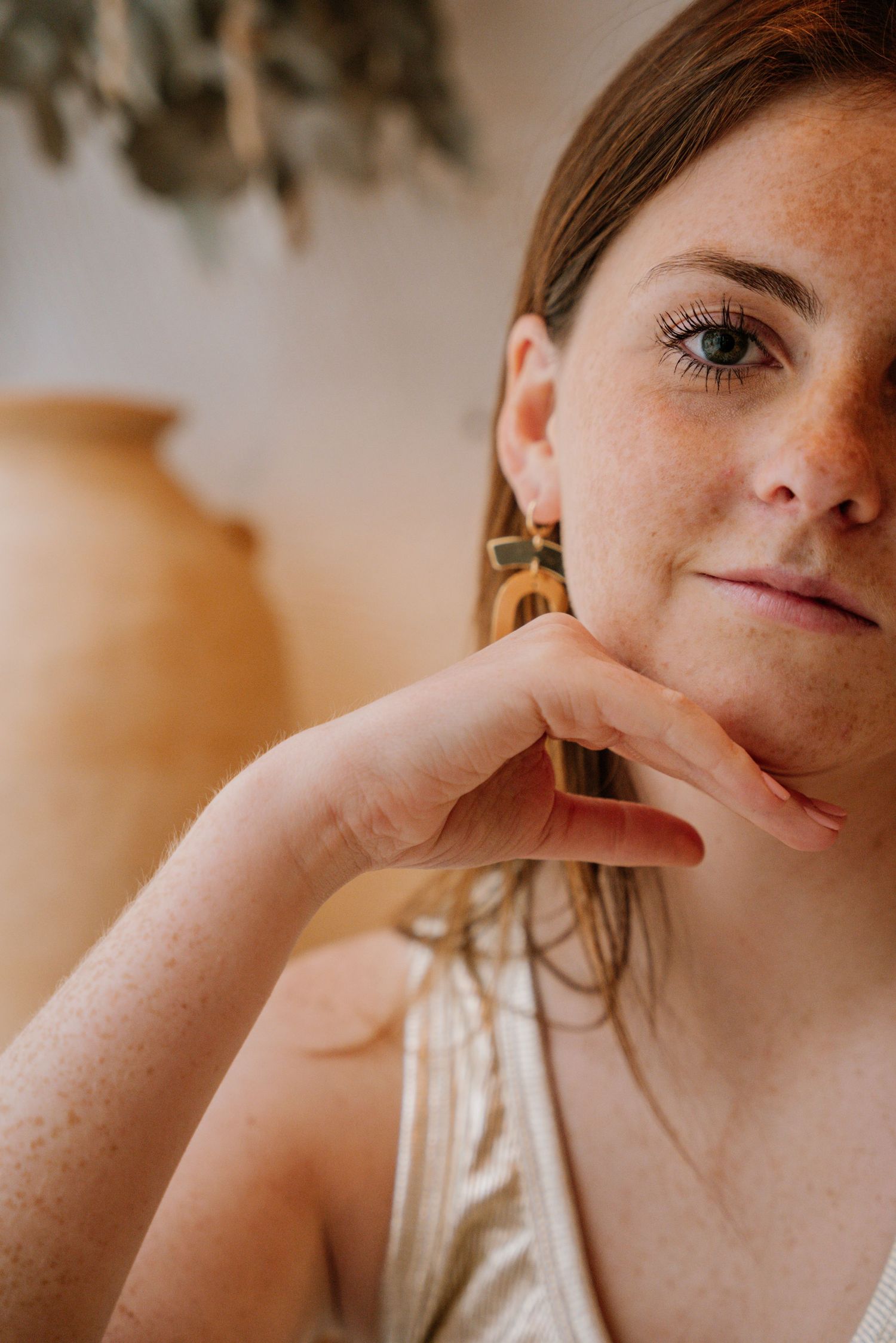 A close-up portrait with freckles and gold earrings in warm lighting against a neutral background.