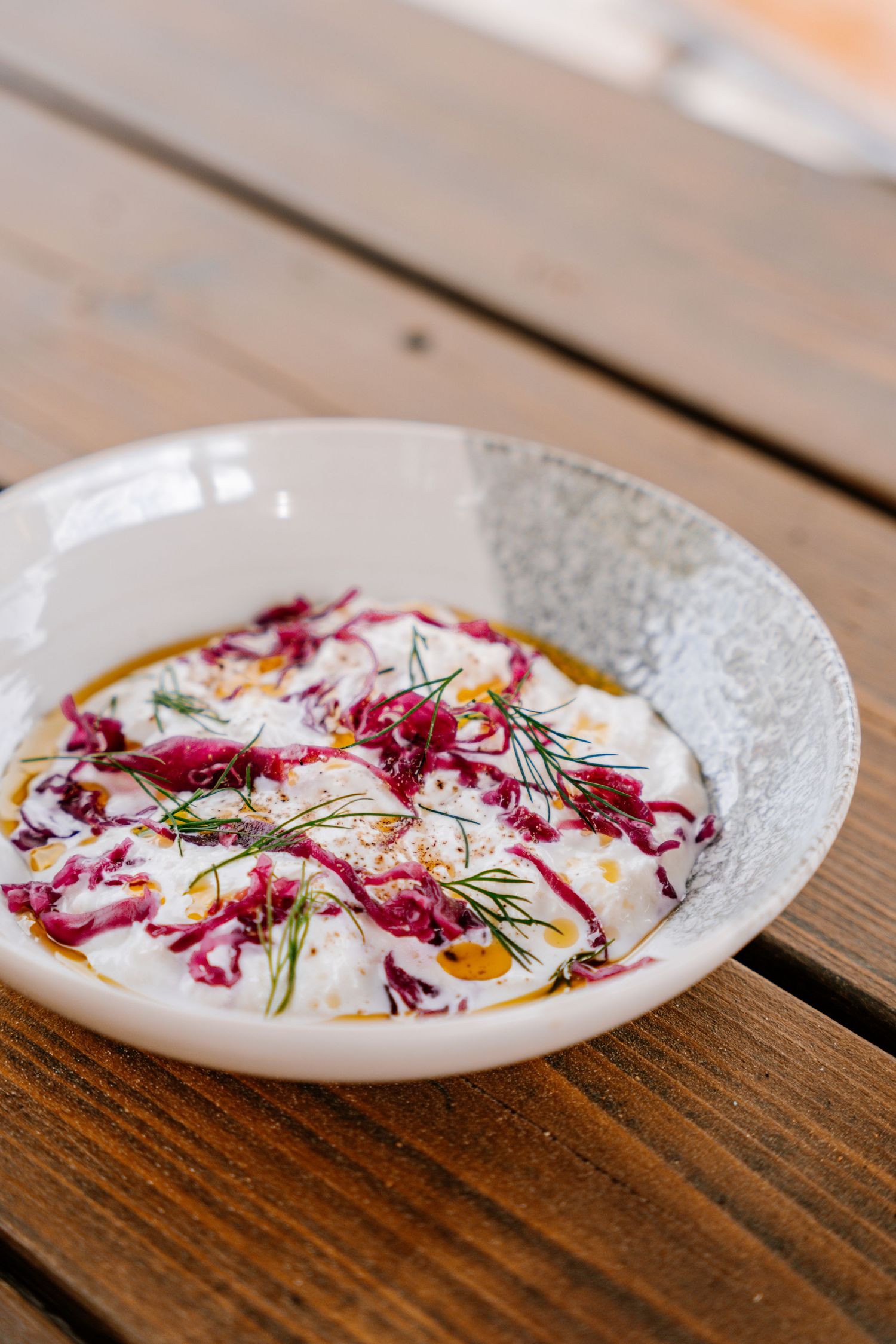 A white plate with fresh sliced radishes, purple cabbage, and fresh herbs arranged artistically on a wooden table.
