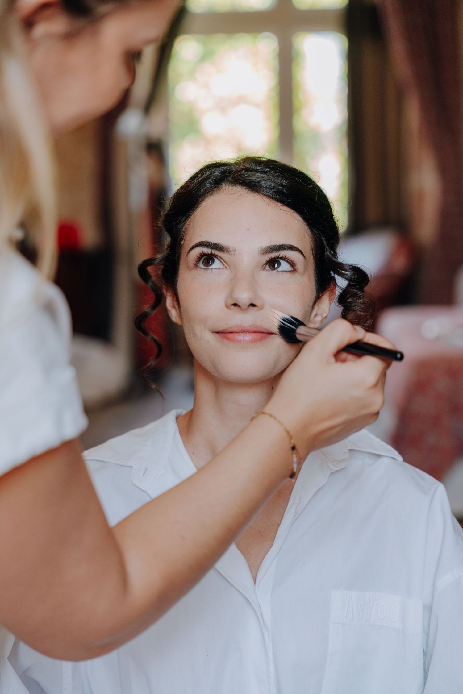 Close-up of makeup application during wedding preparations in natural light.