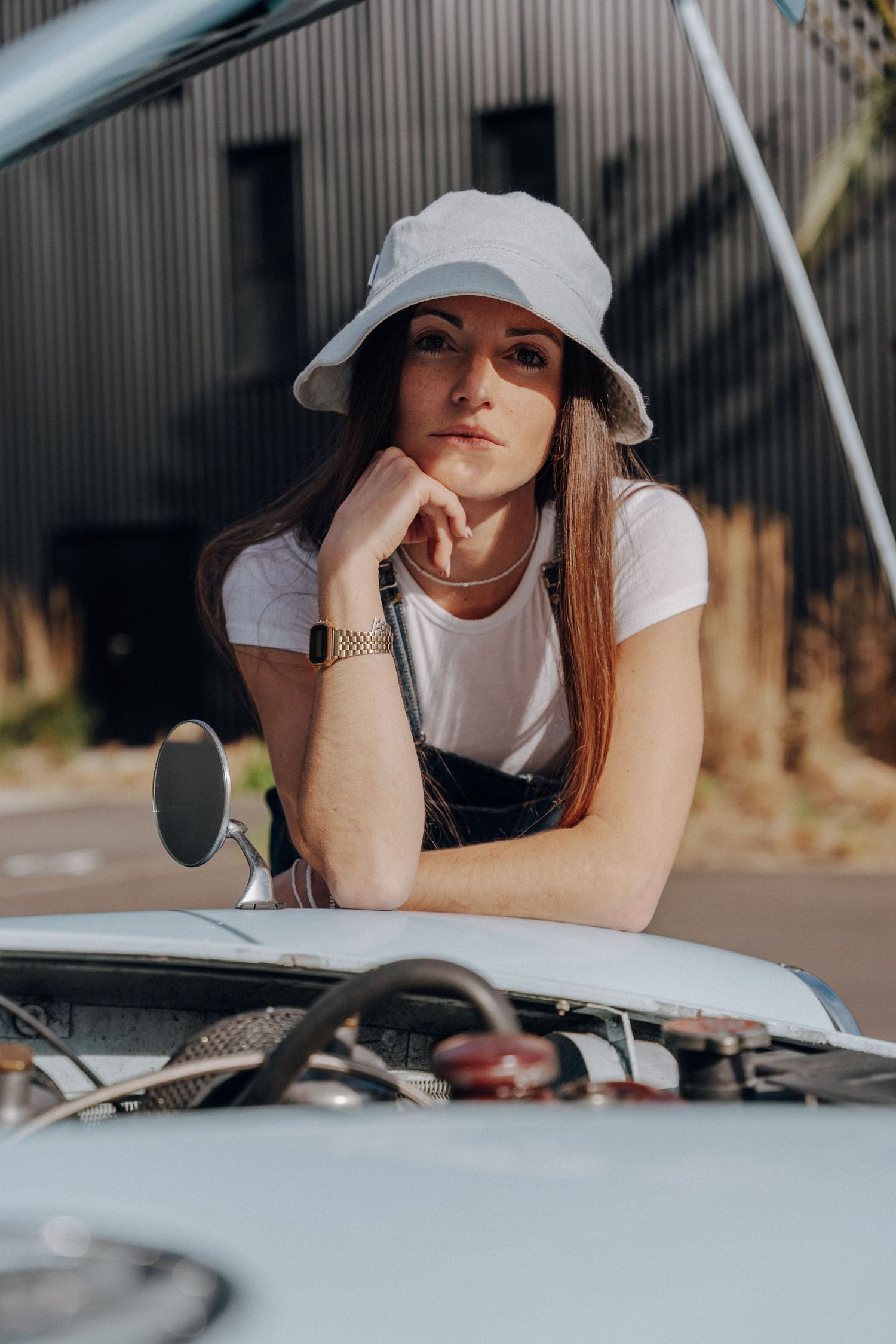 Casual outdoor photoshoot with person in sun hat resting on vintage car.