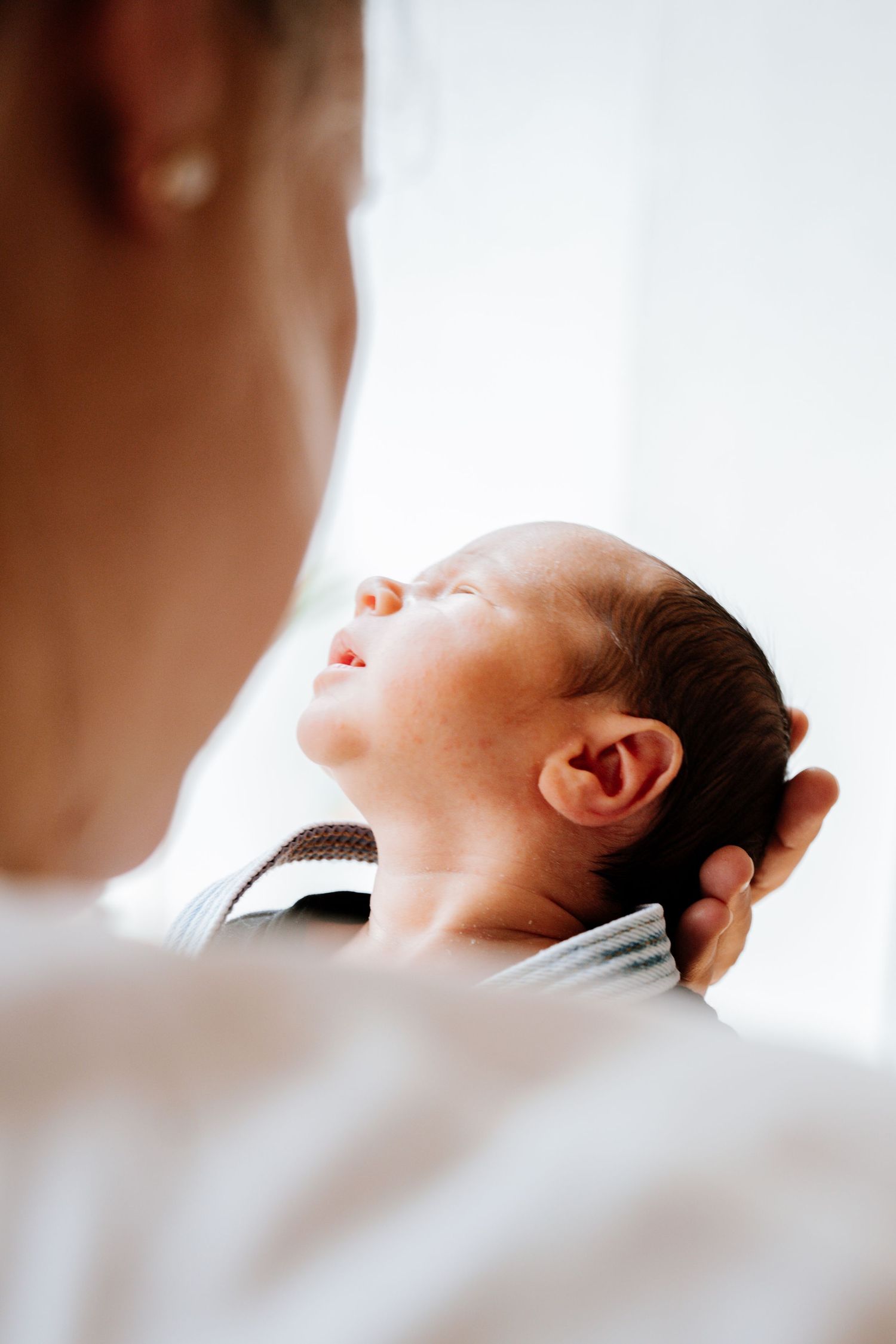 A newborn baby sleeps peacefully in soft natural window light with a blurred silhouette in the foreground.