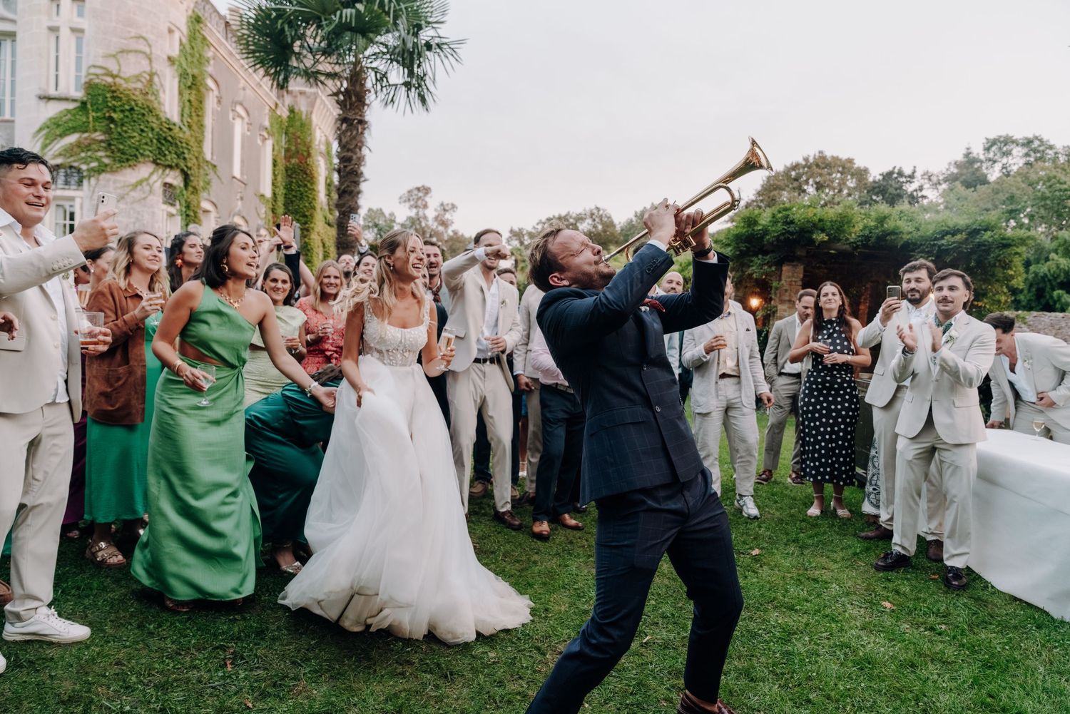 Large group of wedding guests celebrating outdoors with joyful expressions.