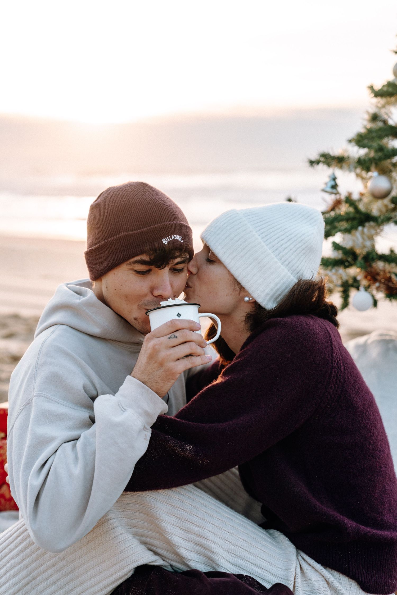 Winter beach scene with Christmas tree and intimate moments at sunset.