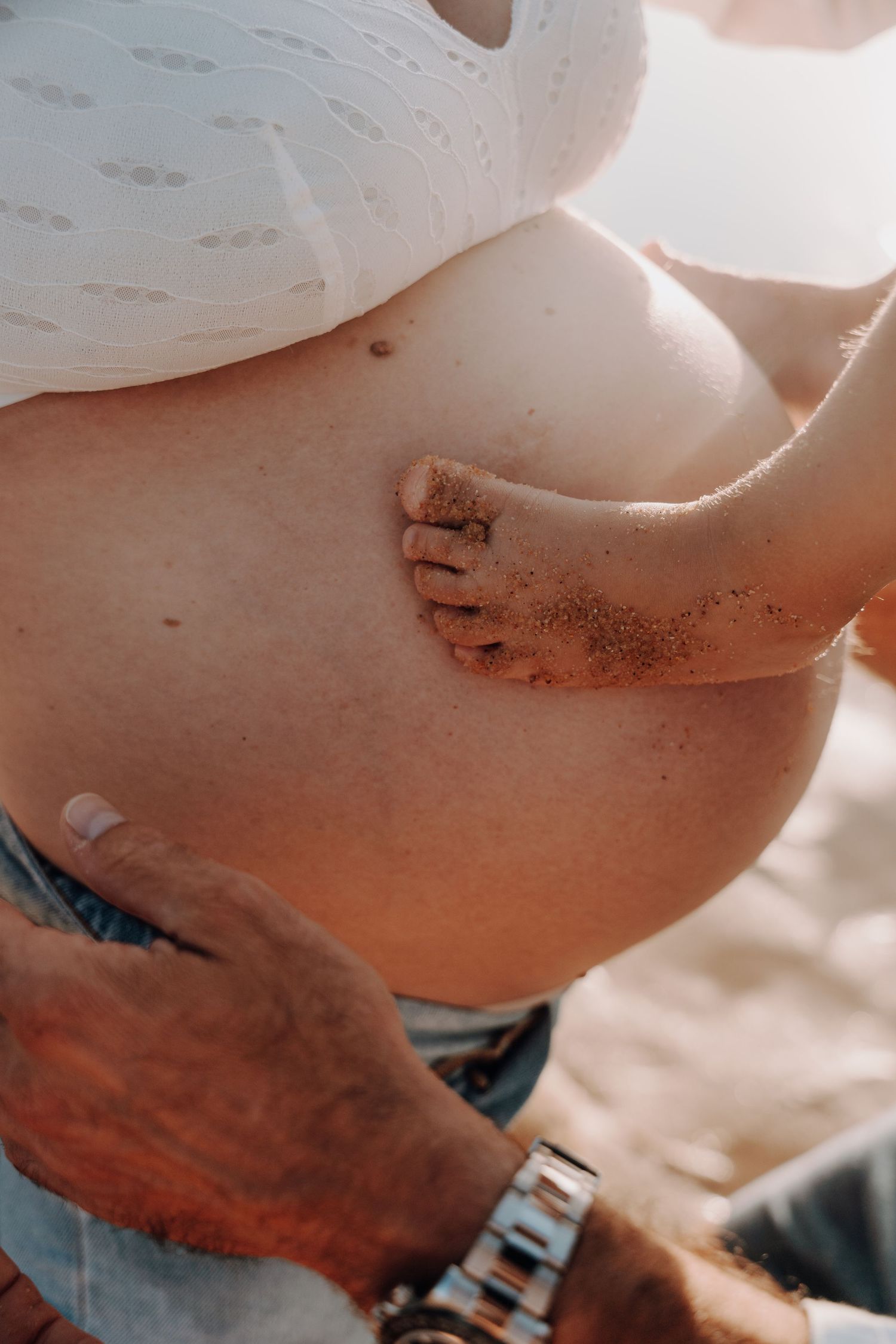 Close up view of pregnant belly being lovingly touched on beach.