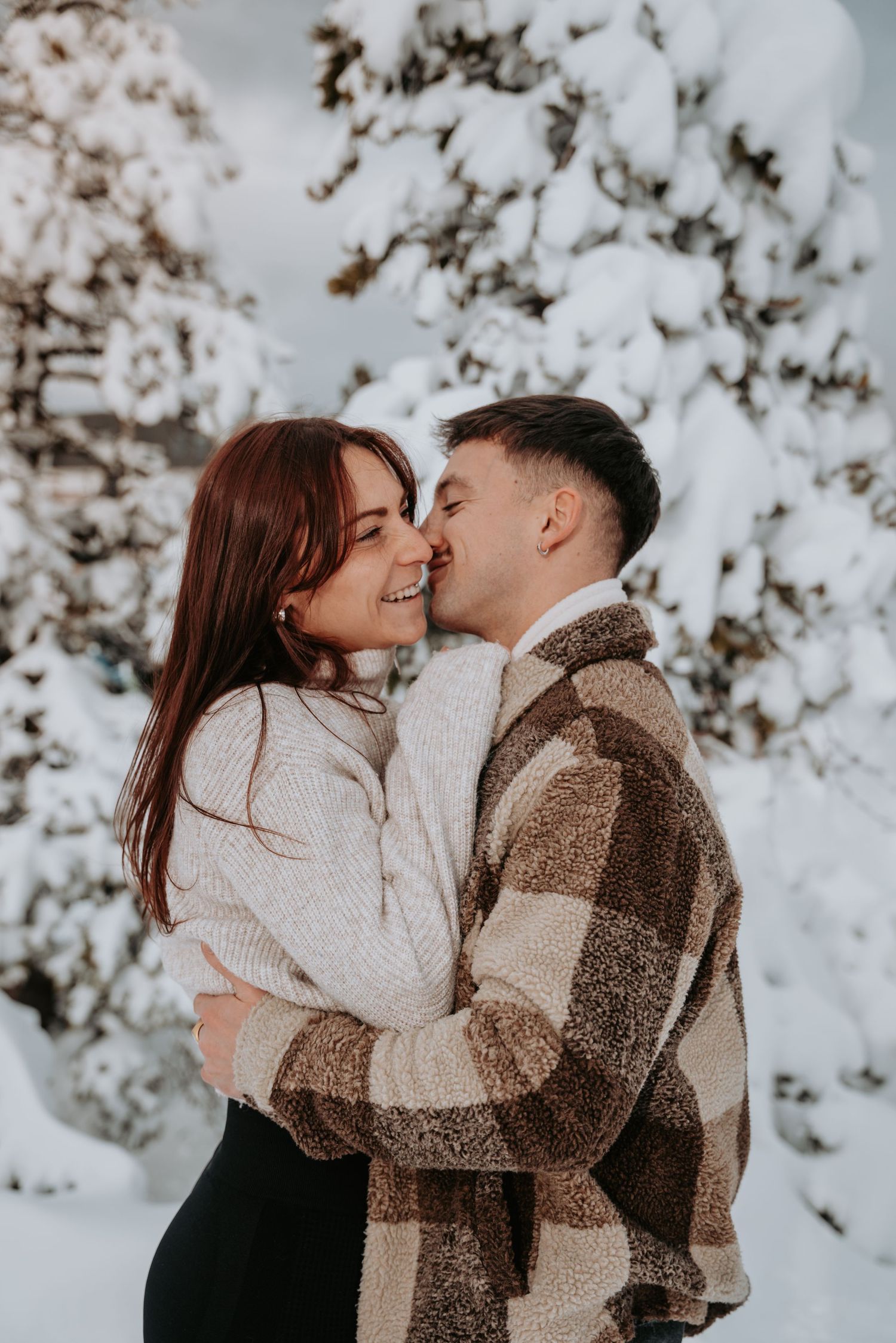 A romantic winter photoshoot featuring a couple in cozy sweaters against a snowy backdrop.