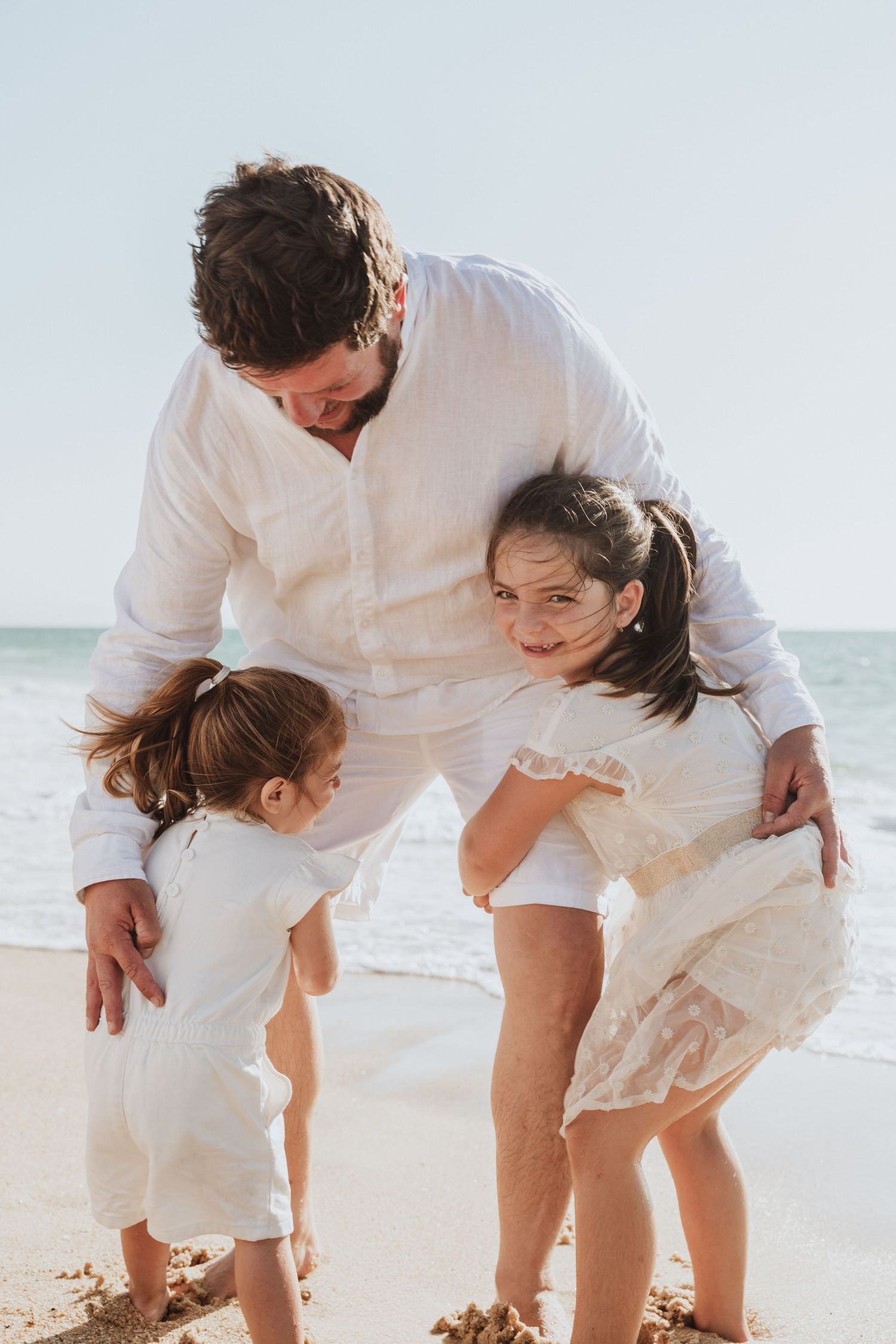 Family in white clothing playing together on sunny beach.