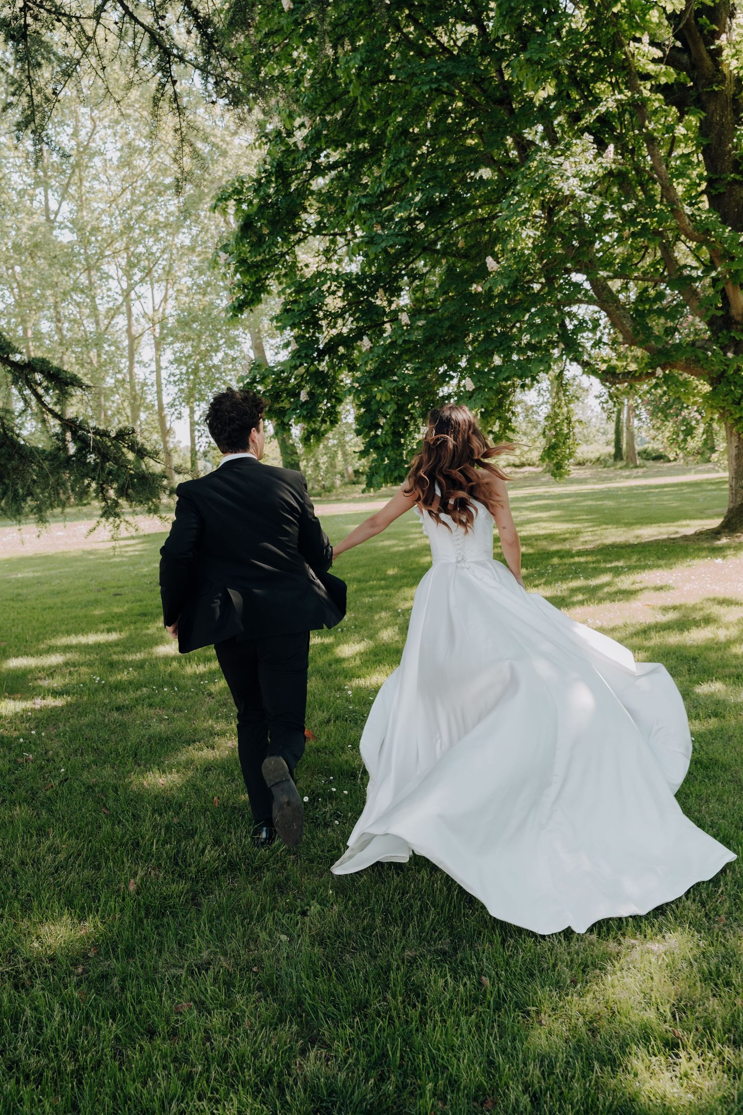 Newlyweds running playfully across a sunlit grassy lawn.