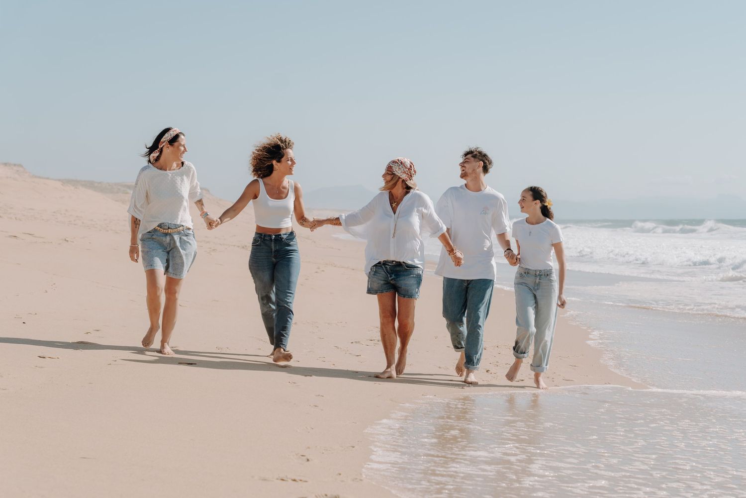 Group walking together hand in hand along scenic beach shoreline.