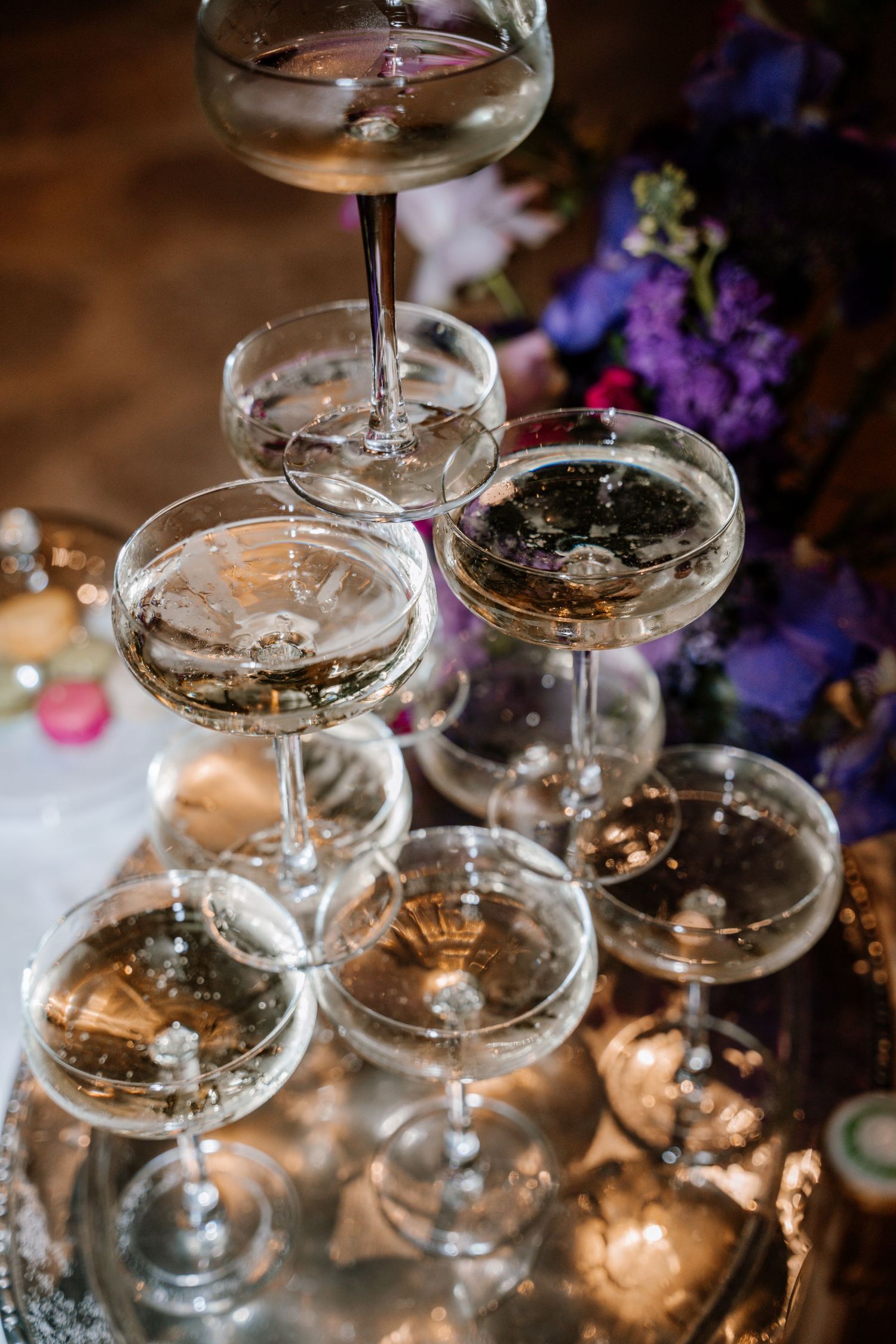 Vintage champagne coupes stacked in pyramid formation with purple flowers in background.