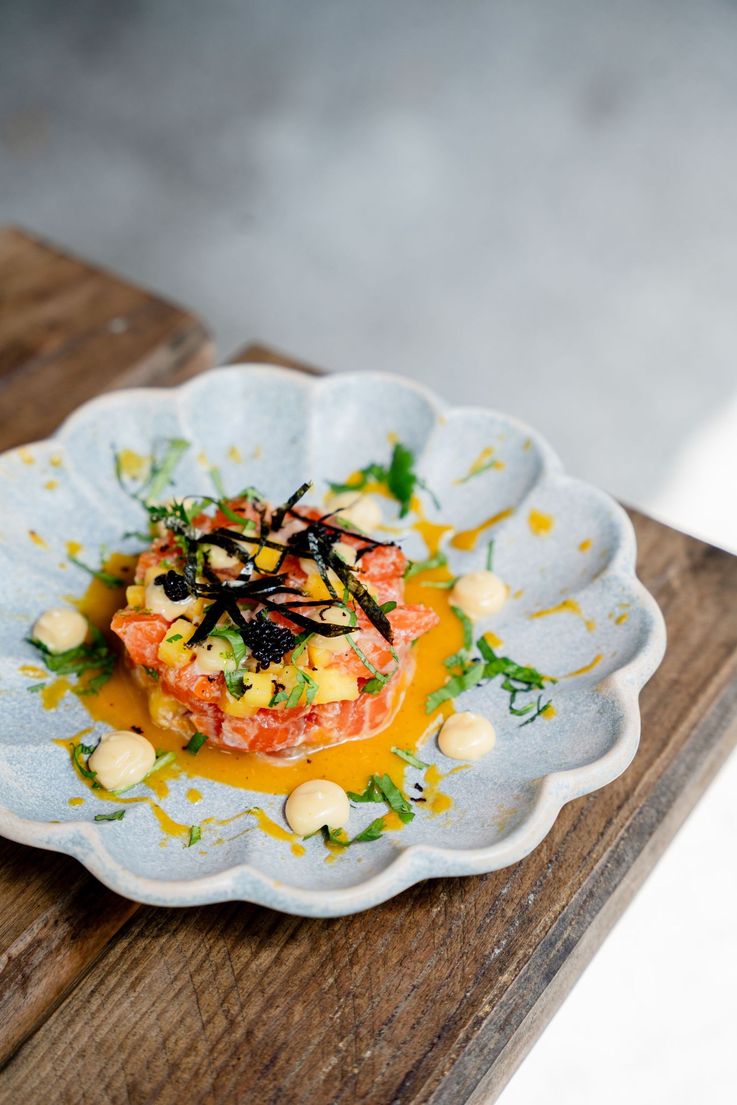 Beautifully plated salmon dish with garnishes on a decorative white flower-shaped plate against rustic wood background.