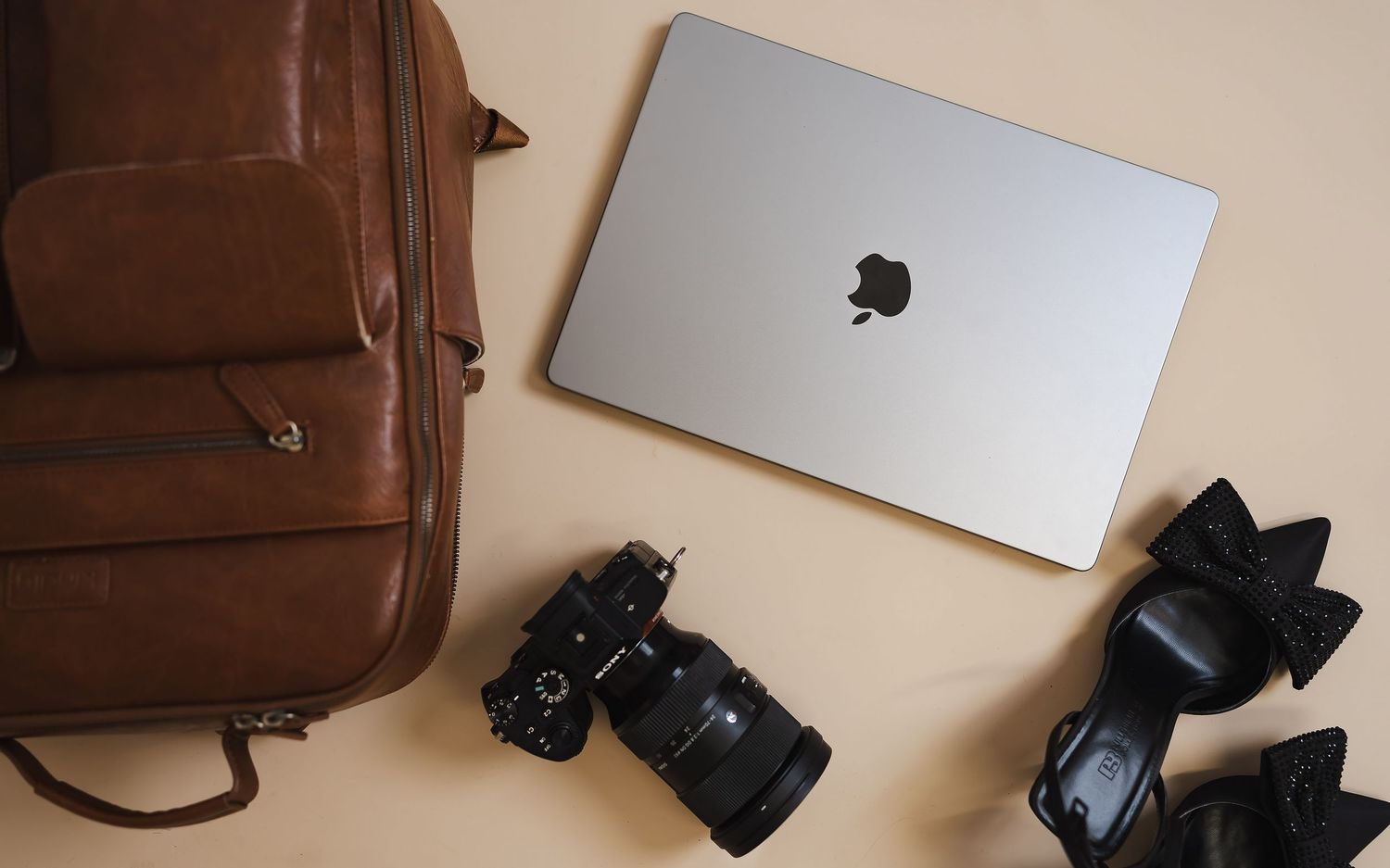 Flatlay of photography equipment including laptop, camera, and brown leather bag.