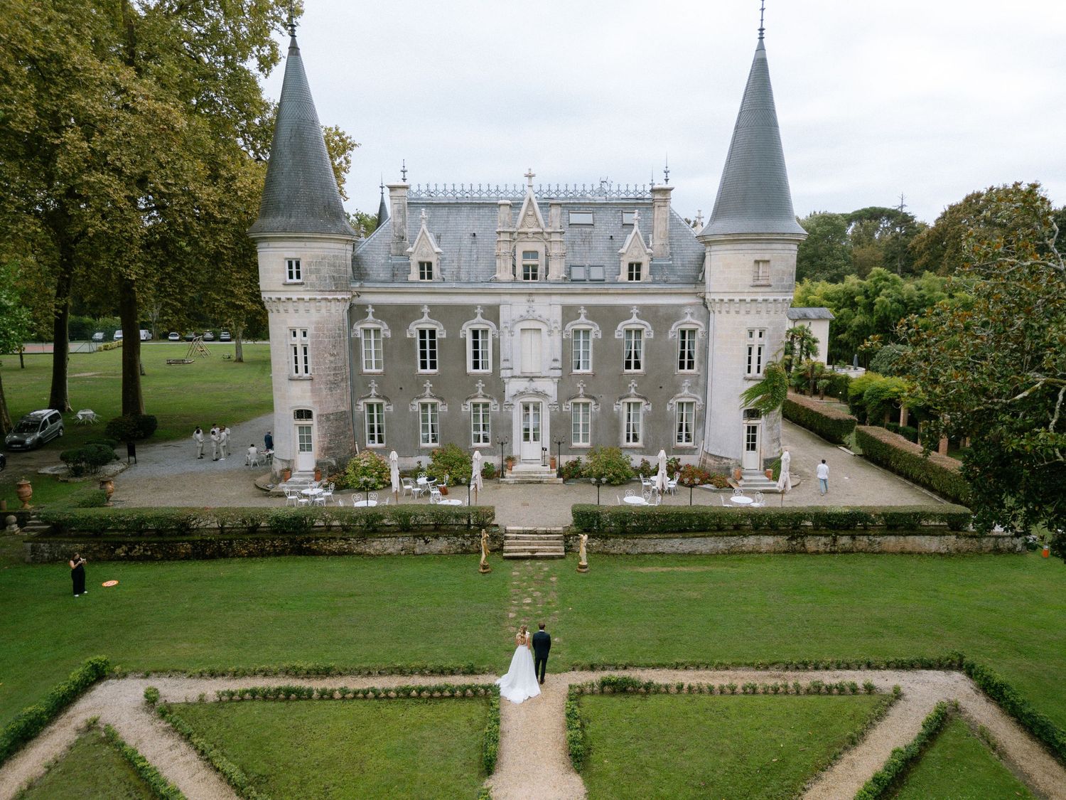 Aerial view of elegant French chateau with manicured gardens and wedding ceremony.