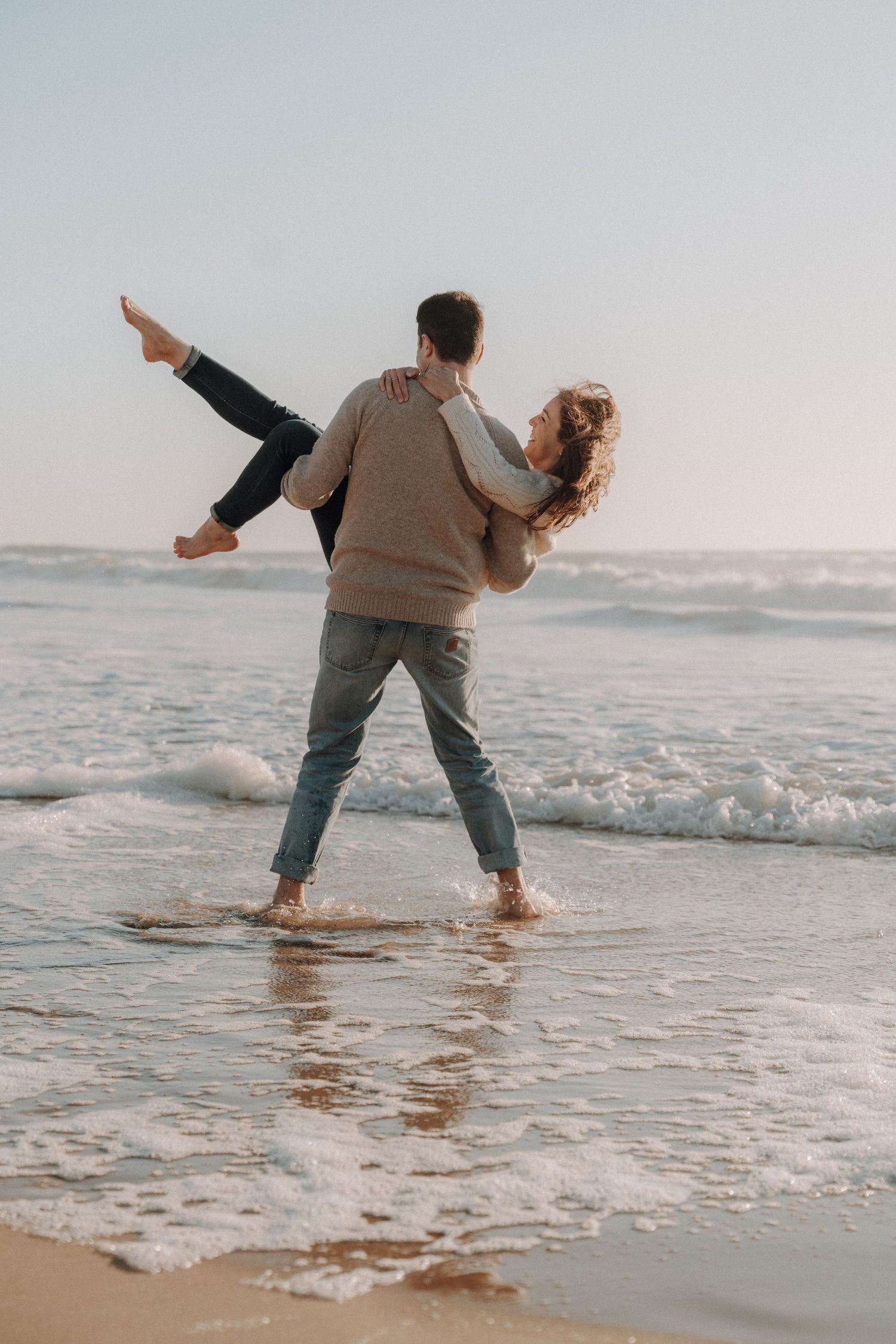 Two people playfully dance together in the shallow ocean waves at sunset.