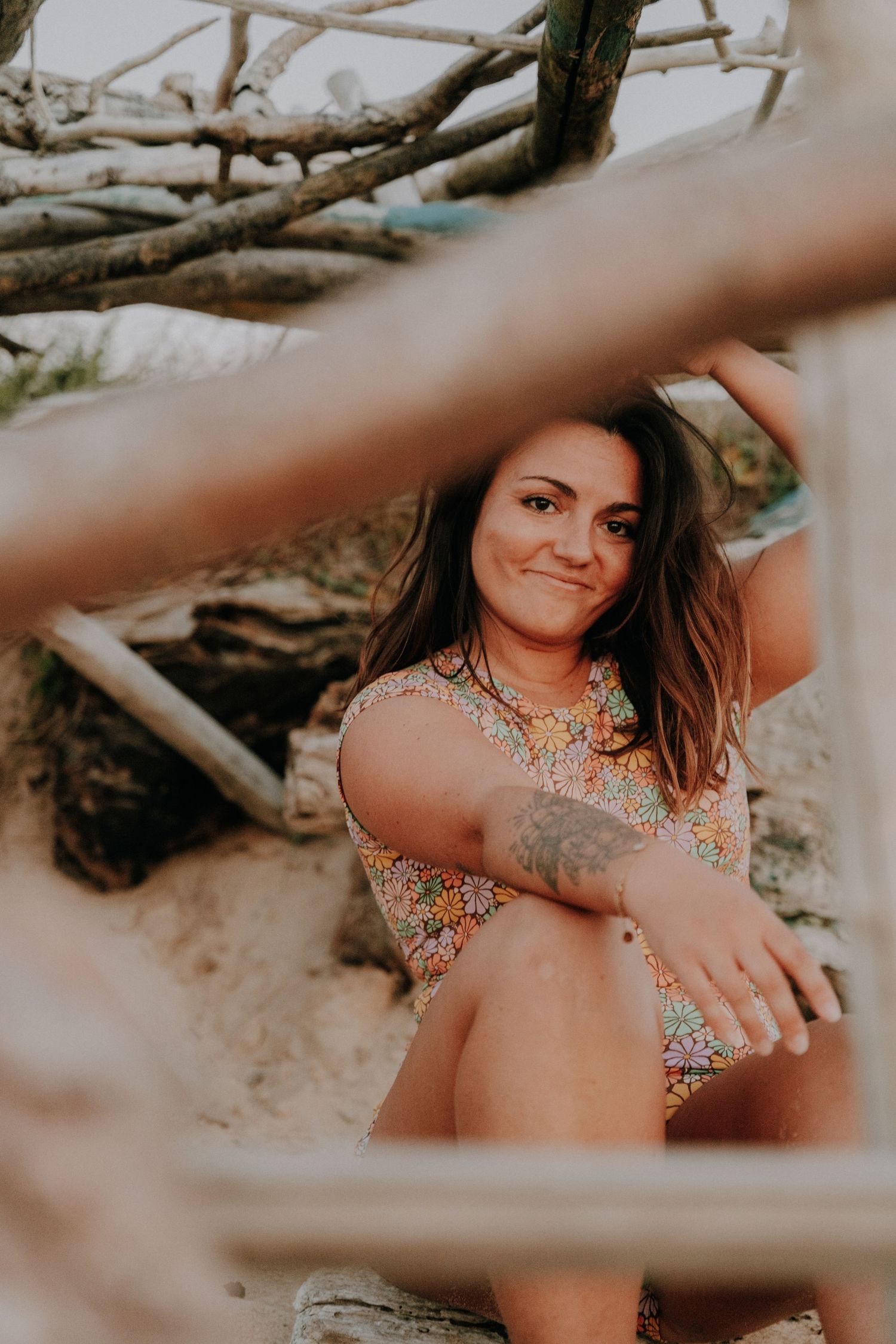 Artistic beach portraits through driftwood featuring someone in a floral swimsuit.